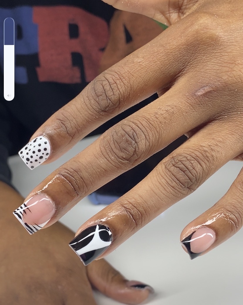 Close-up of a hand with decorated nails, featuring polka dots, black and white designs, and a clear base, with skin visible.