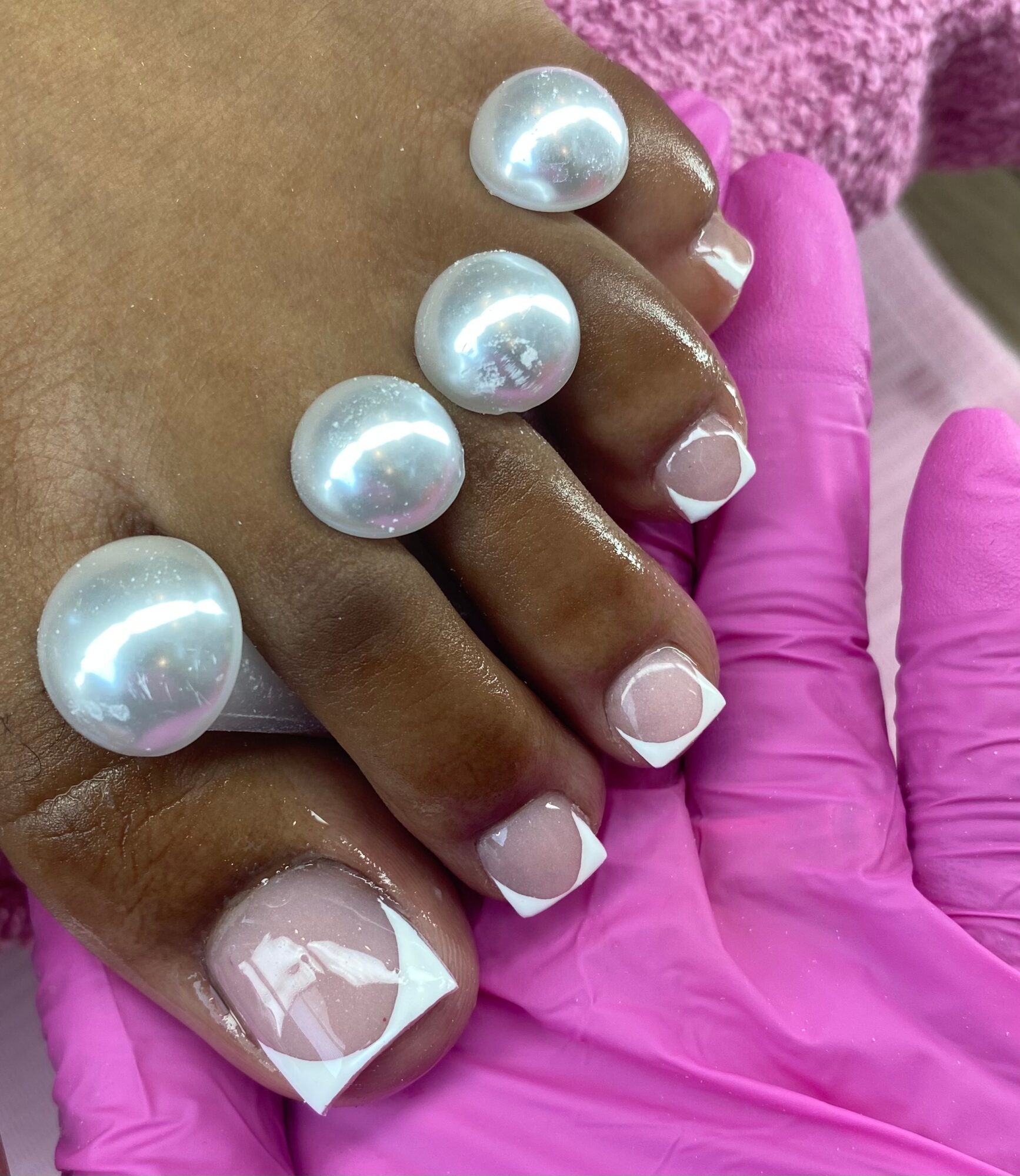 Hand with pearl-like nail art and a pink glove, close-up view of fingers and nails, background pink fabric.