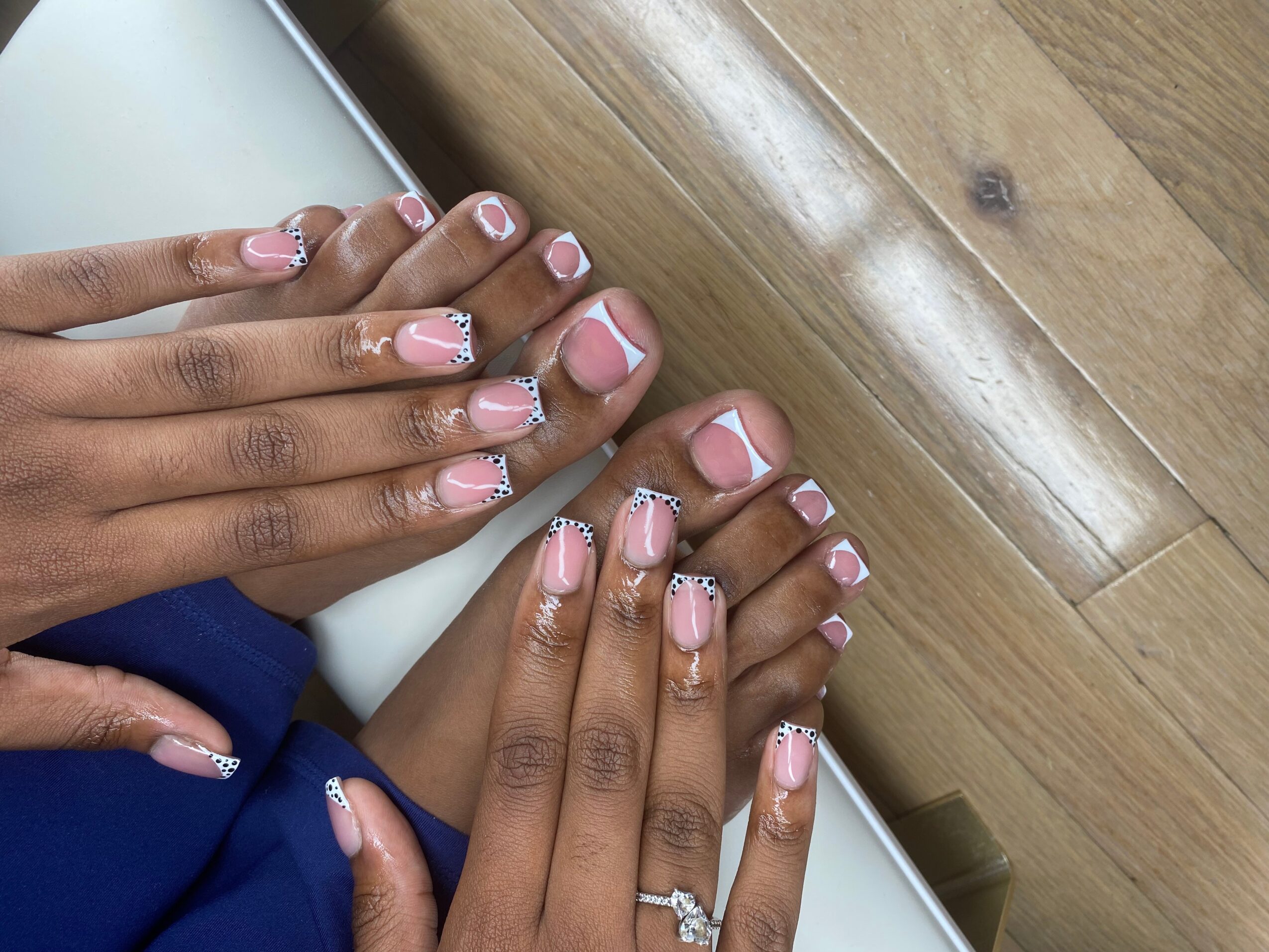 Person with decorated fingernails and toenails, holding a white object, on a wooden surface.