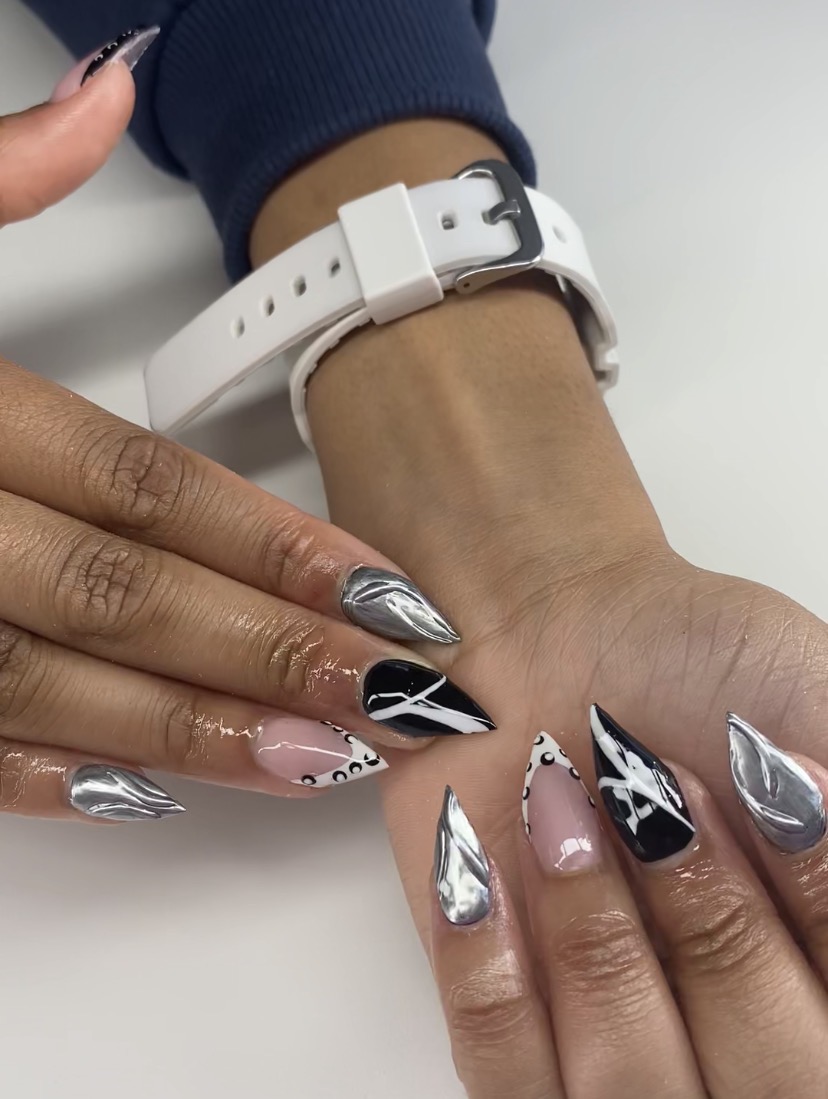 Person's hand with metallic silver and black nail polish, wearing a white watch and a blue sleeve, resting on a white surface.