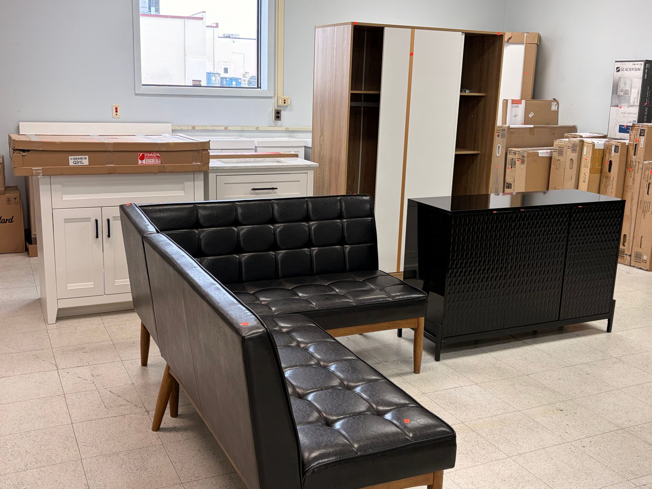 Upright view of a black leather sofa with tufted cushions in a room with white cabinets and cardboard boxes.