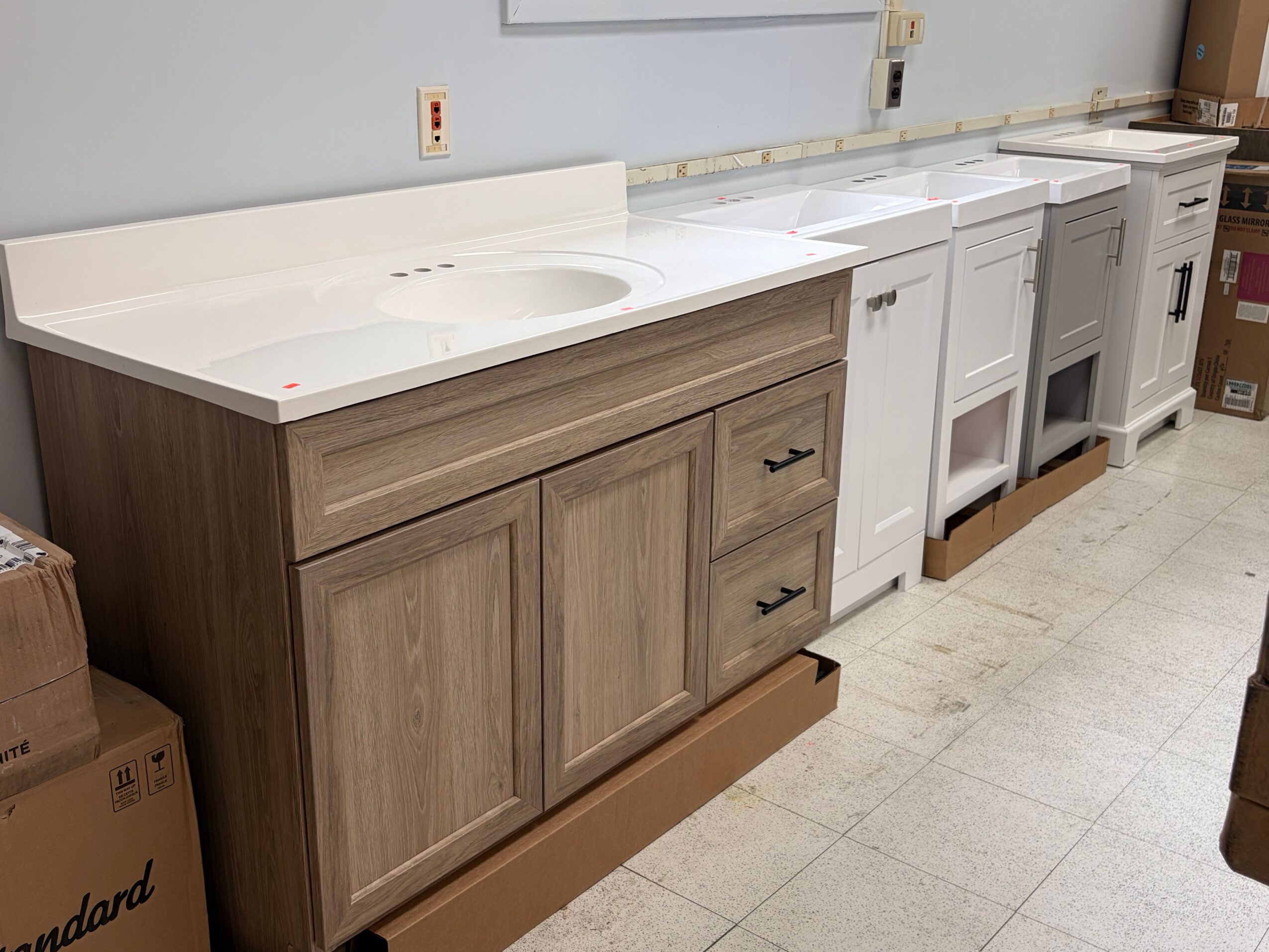 Wooden kitchen cabinet with drawers and doors, under a beige countertop, with a white range hood below, in a store setting.