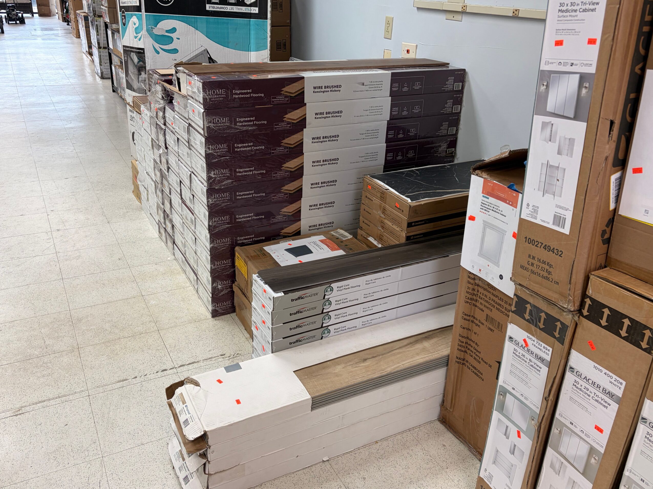 Stacked boxes and packages on a warehouse floor, some with labels and barcodes, viewed from the side.
