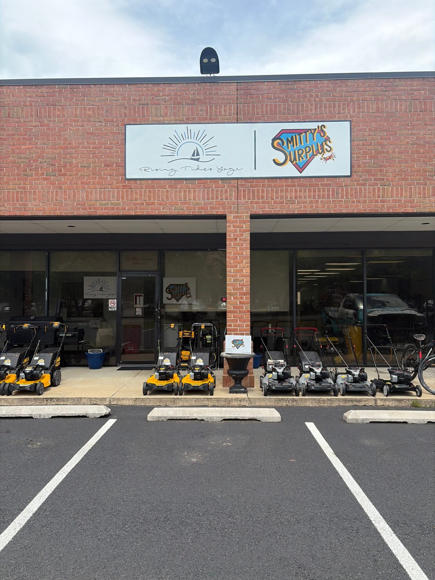 Storefront with a brick facade, sign, and bicycles parked outside, viewed from the side. Parking lot with white lines.