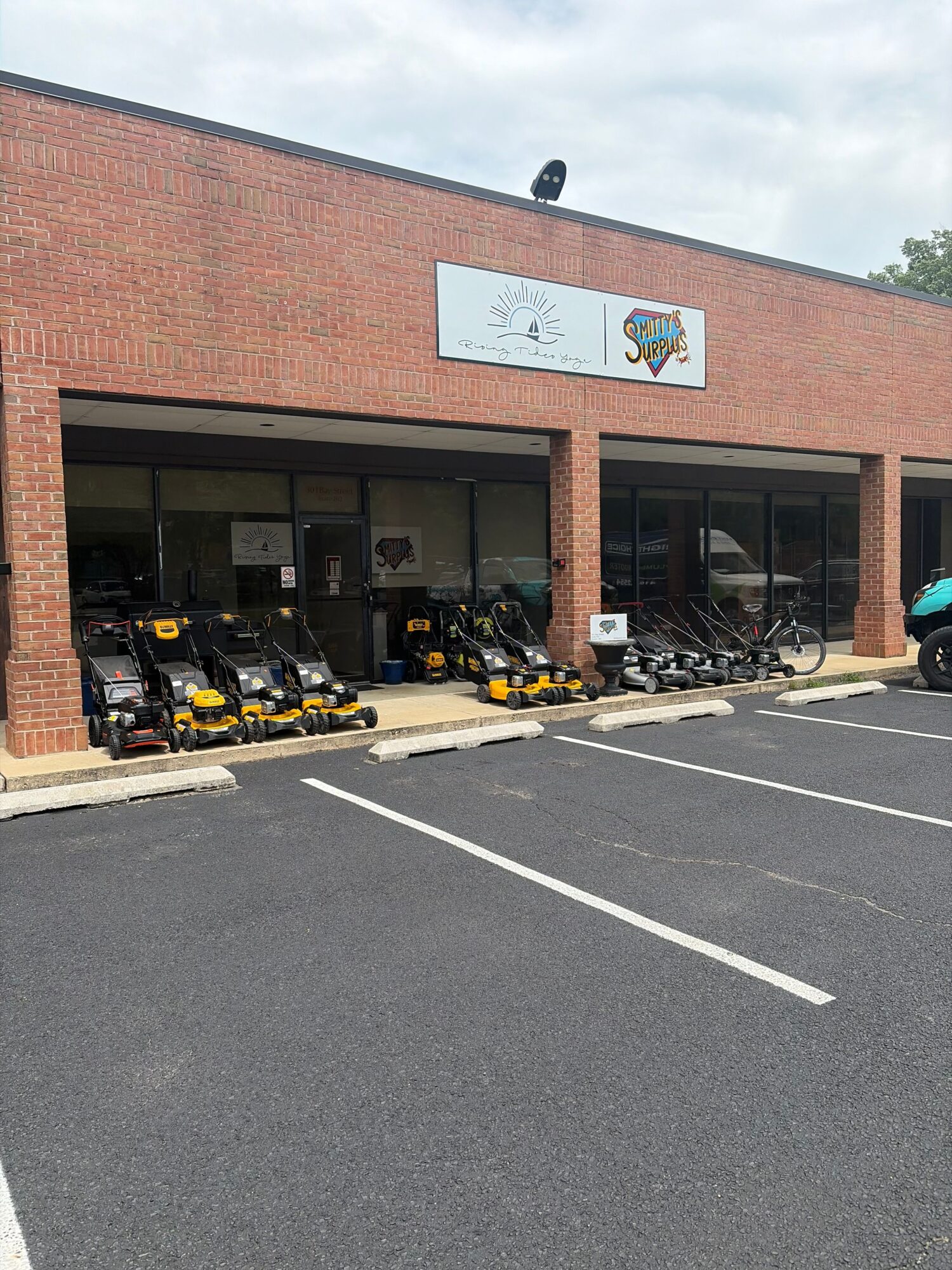 Bicycle parking area outside a brick building with a sign, bicycles, and a parking lot.