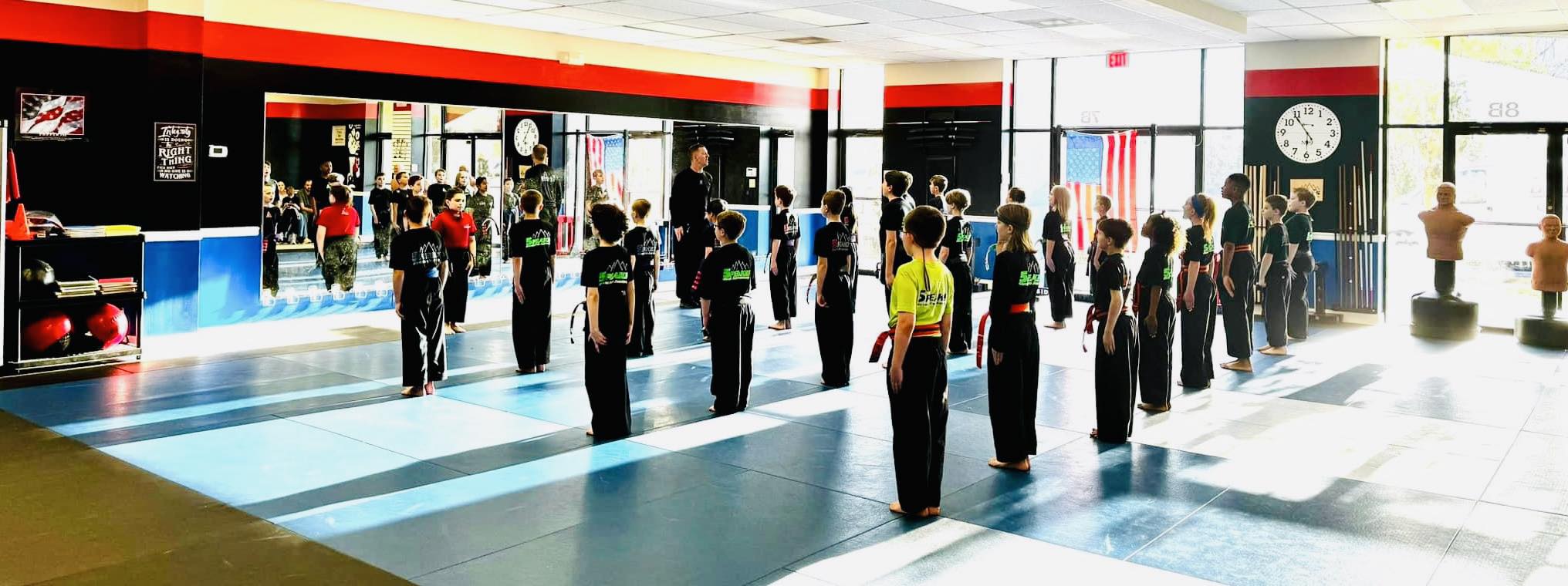 People practicing martial arts in a spacious, well-lit indoor training area with mats and large windows.
