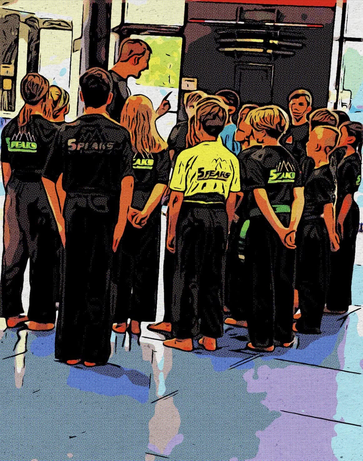 Group of children in martial arts uniforms standing in a line indoors, with a woman instructing them, colorful floor and windows.