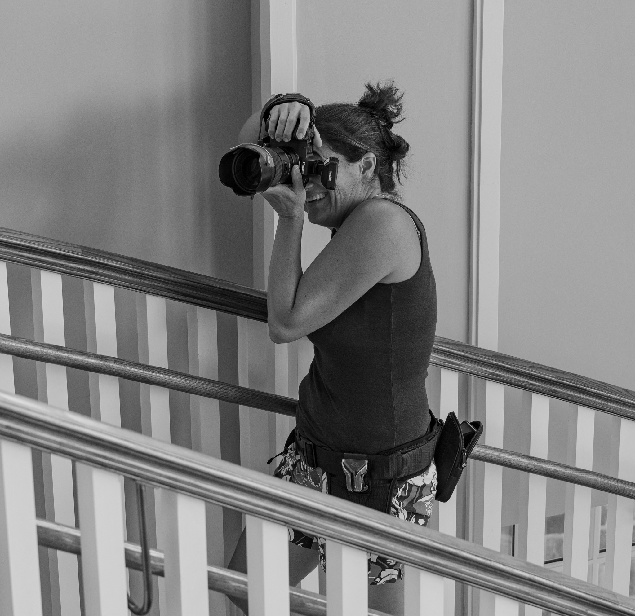 Woman with a camera taking a photo, standing on a balcony with railing, in black and white.