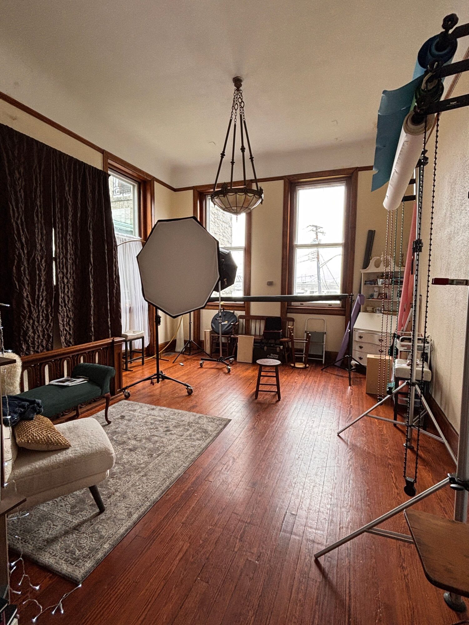 Room with wooden floor, window, and furniture including a chair, table, and a light stand, viewed from a different angle.