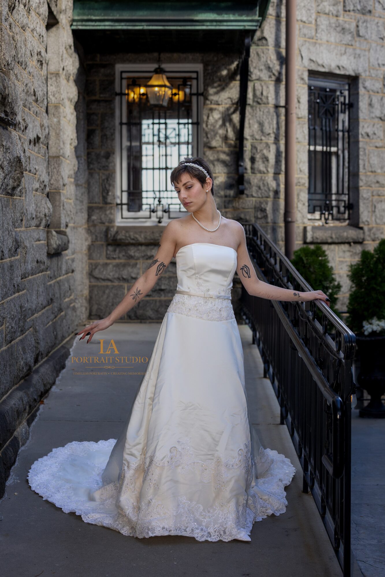 Woman in a white wedding dress standing on a narrow outdoor walkway with stone walls and black railing.