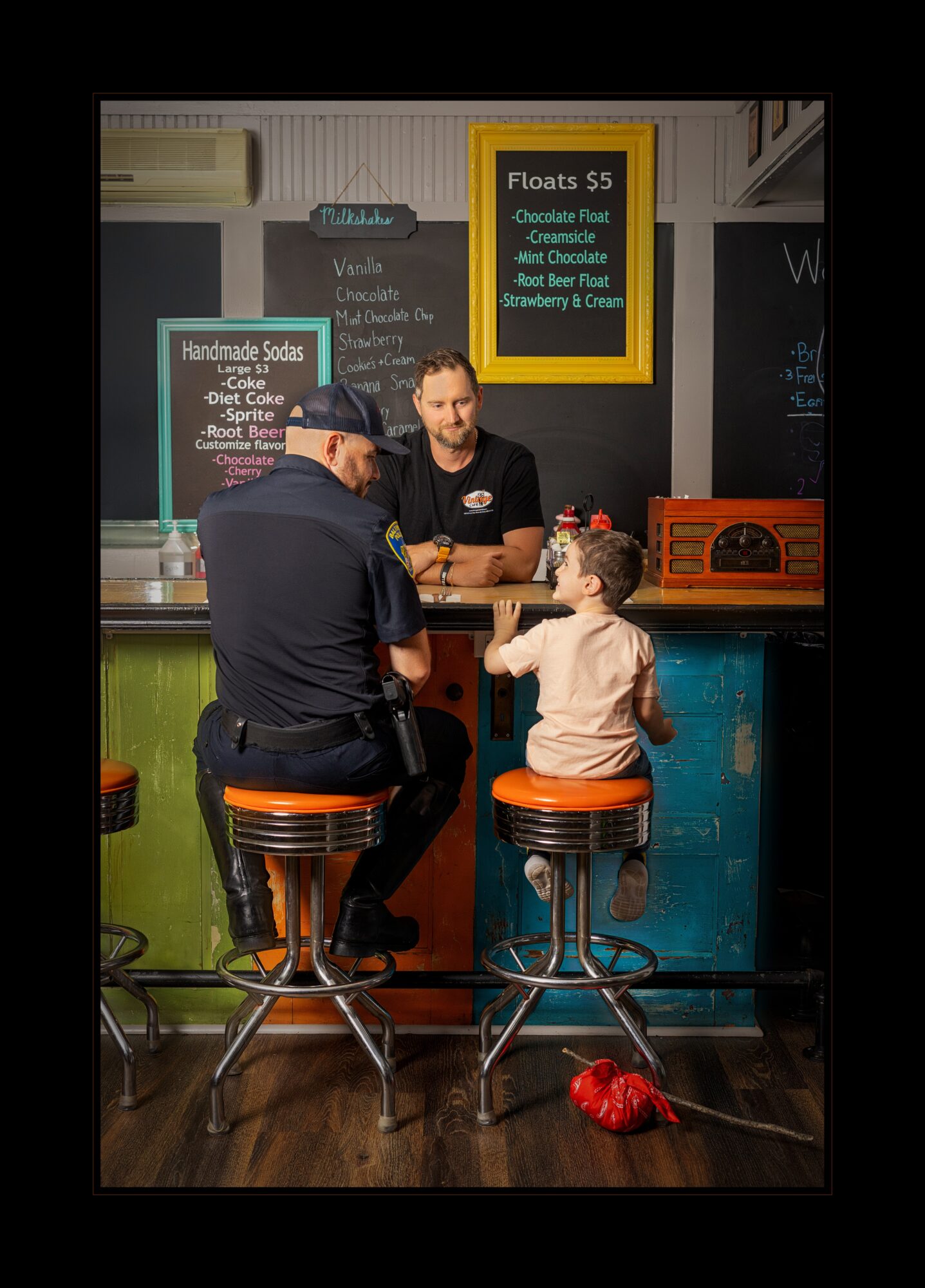 A man and a young girl sit at a counter in a colorful shop, talking to a worker behind the counter.