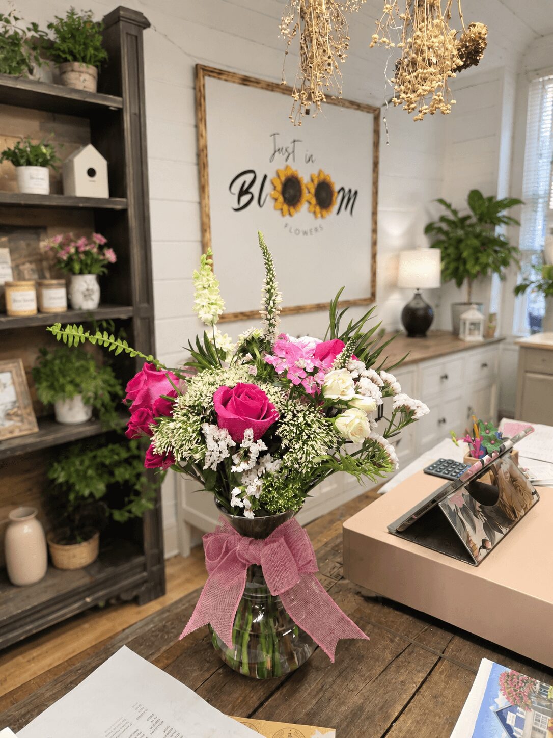 Vase with pink roses, white flowers, and greenery on a wooden table in a decorated room.
