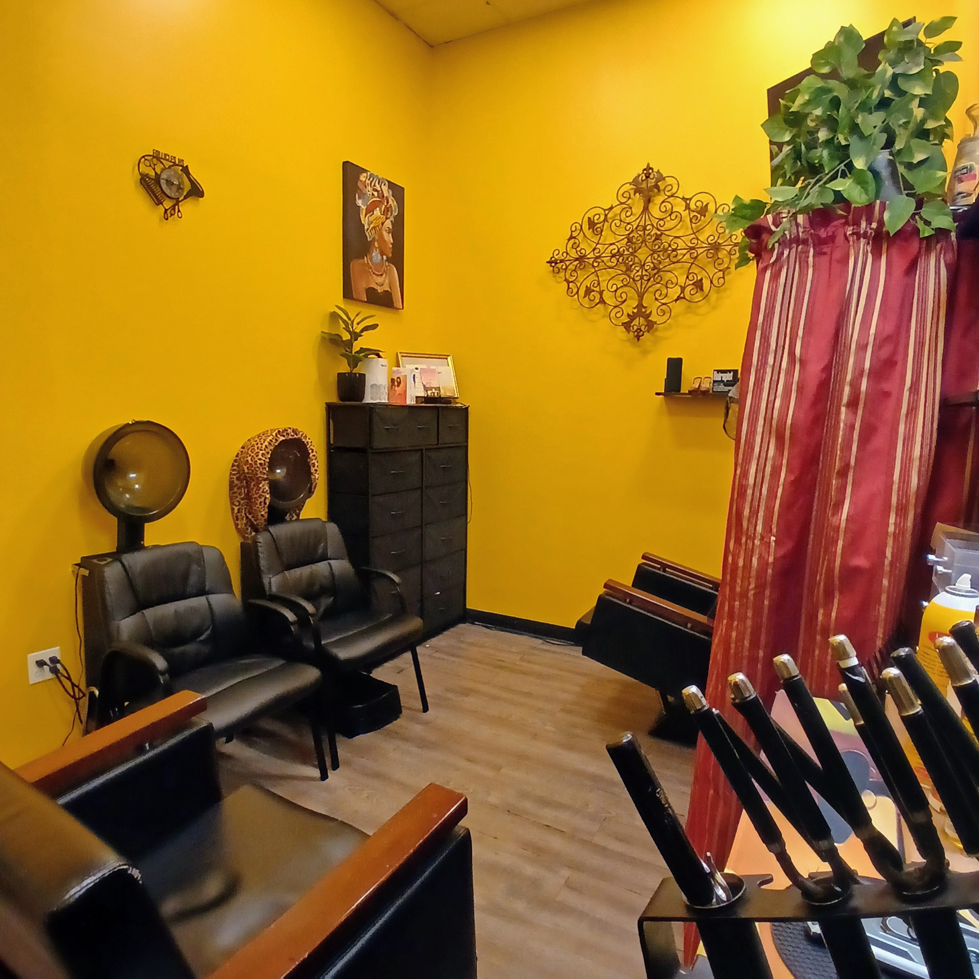 Room with yellow walls, two black chairs, a tall black cabinet, and a red curtain with a plant. Wooden floor.