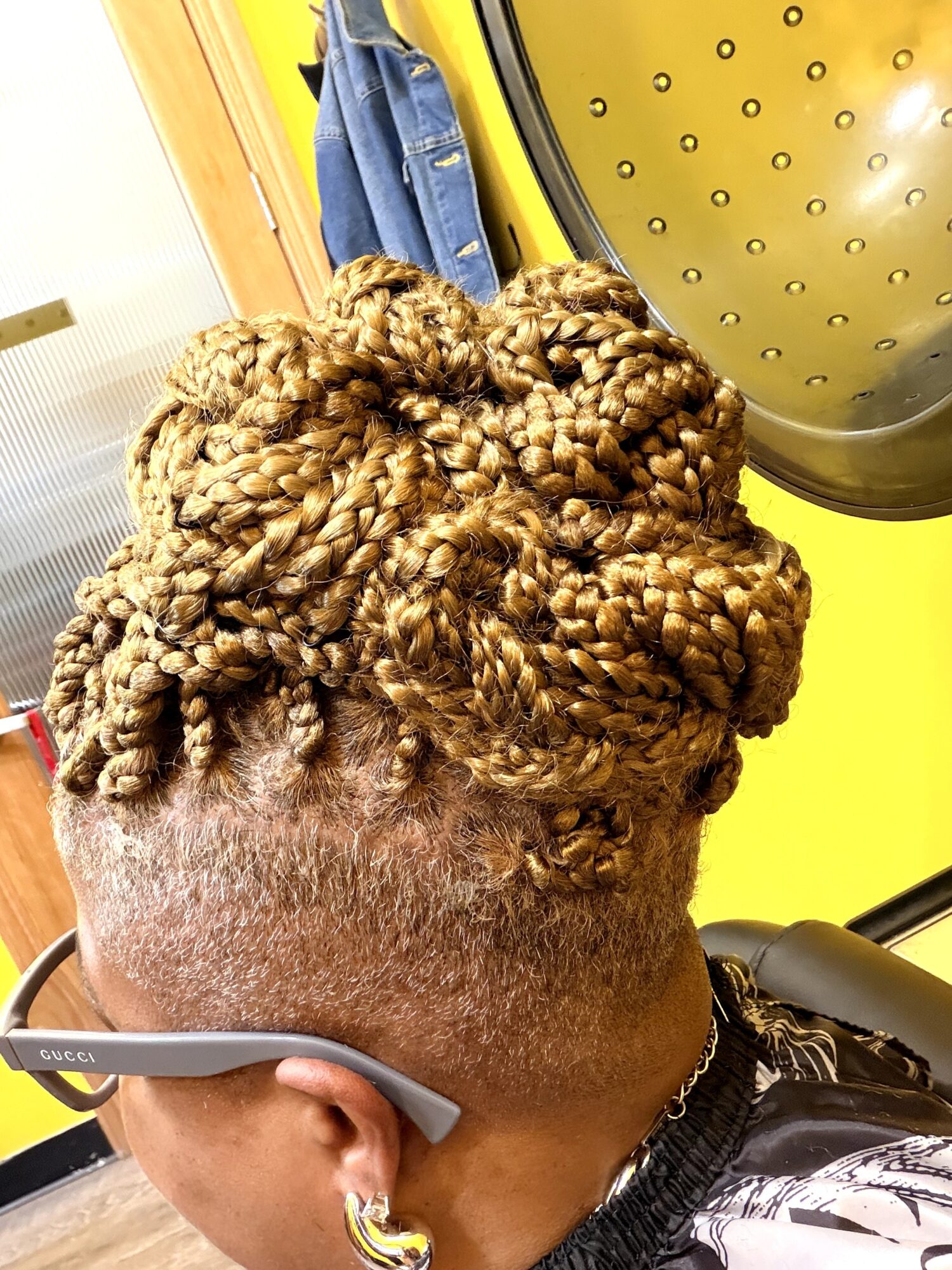 Close-up of a person's head with styled blonde twists and shaved sides, in a salon setting.