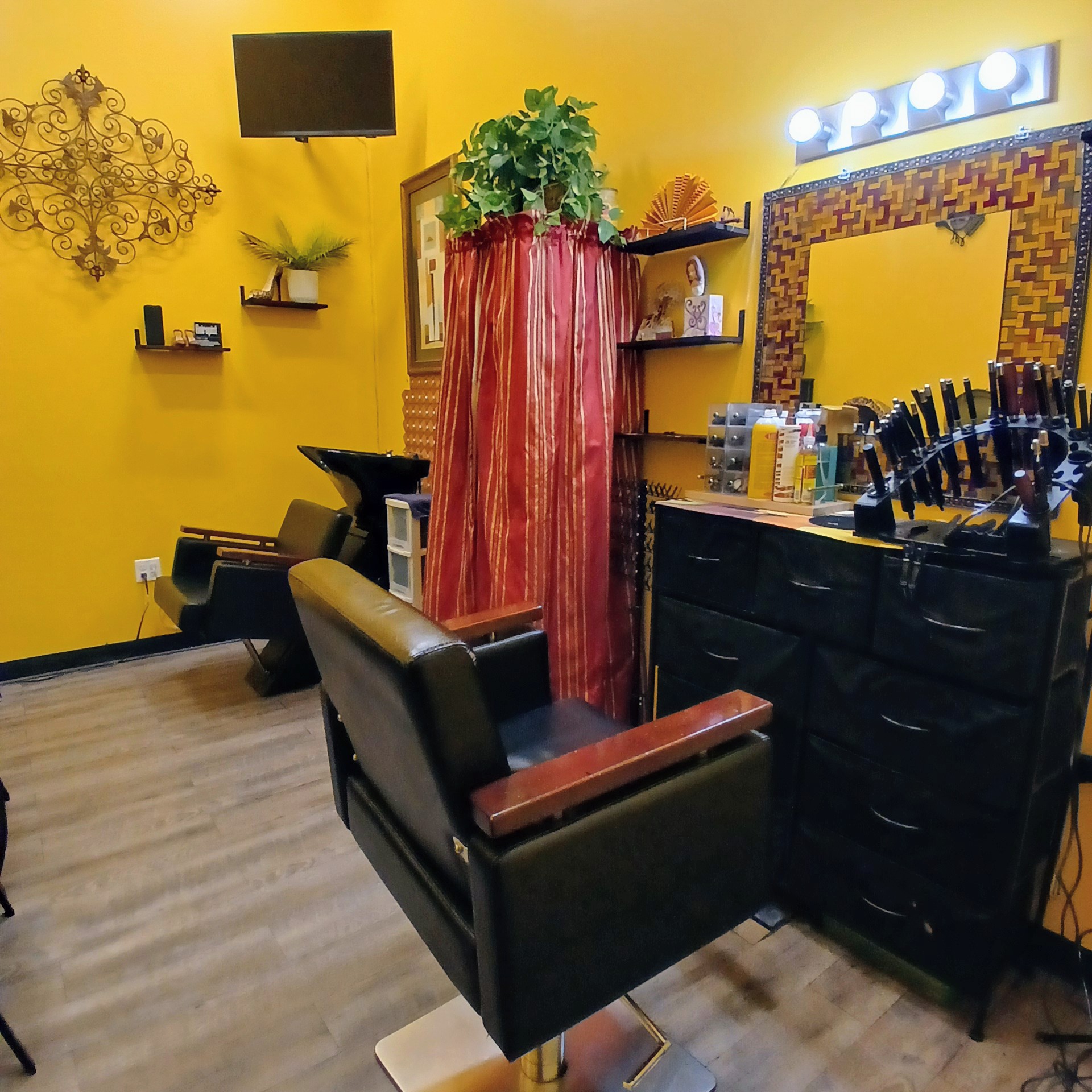Beauty salon with yellow walls, a mirror, styling tools, and a black chair, decorated with plants and wall art.