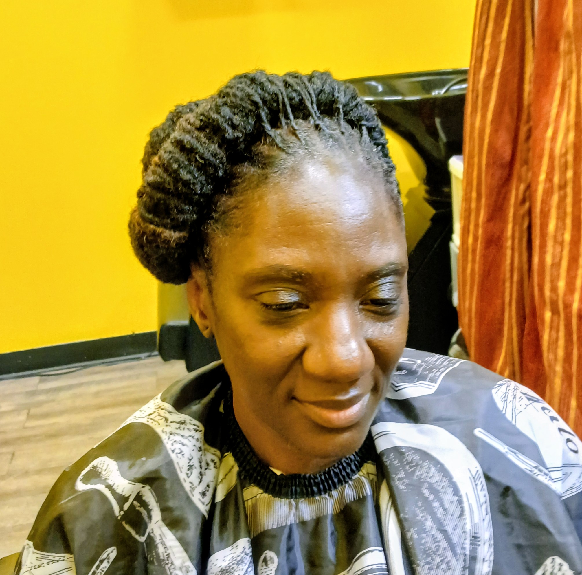 Woman with styled hair sitting in a salon chair, yellow wall and curtain in background.