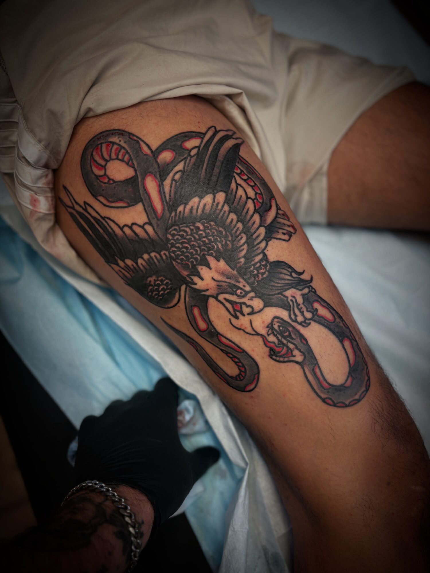 Tattoo of a snake and a bird on a person's thigh, with detailed black and red ink, lying on a bed.