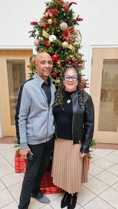 Man and woman standing in front of a decorated Christmas tree, smiling, indoors.
