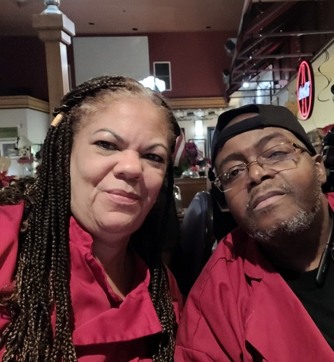 Two people wearing red shirts in a restaurant, smiling at the camera.