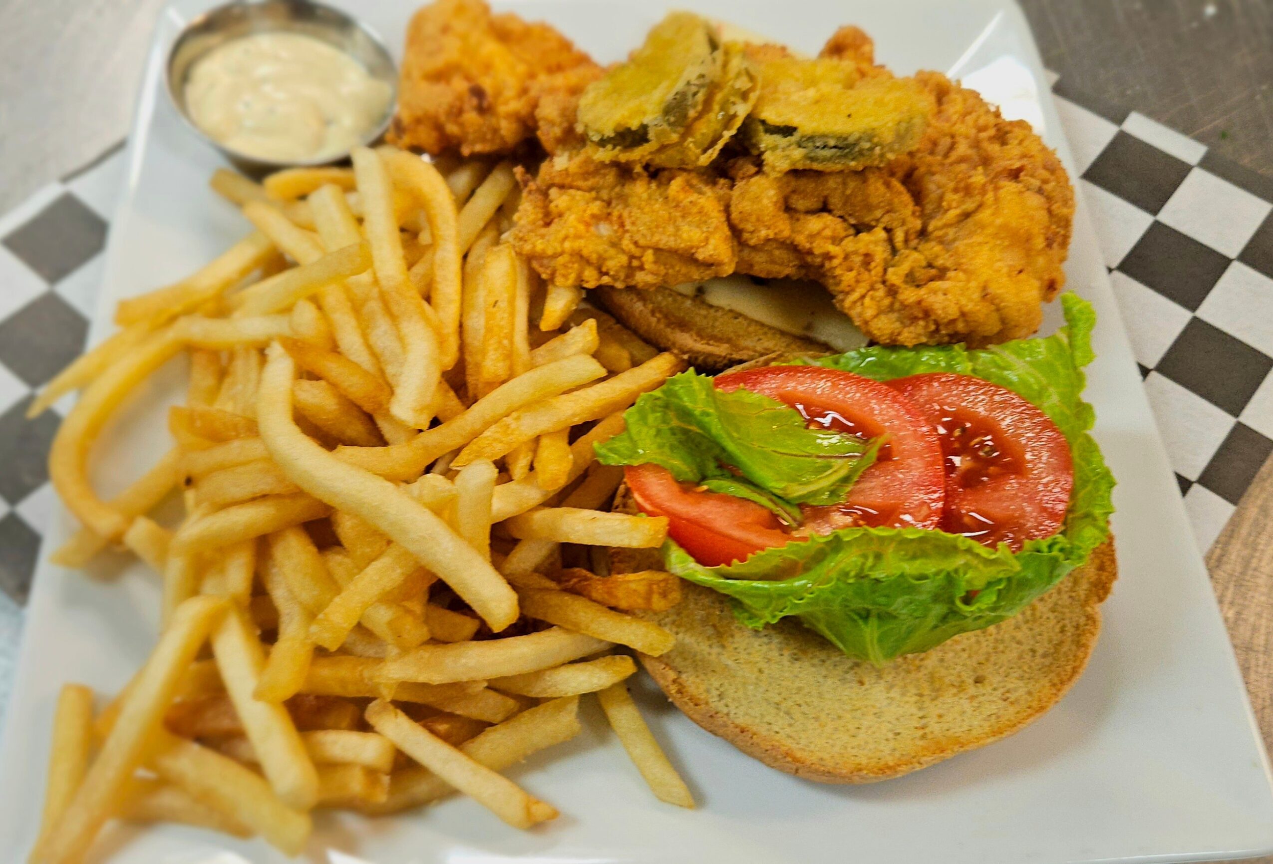 Fried chicken, French fries, and a sandwich with lettuce, tomato, and pickles on a bun, served with dipping sauce.