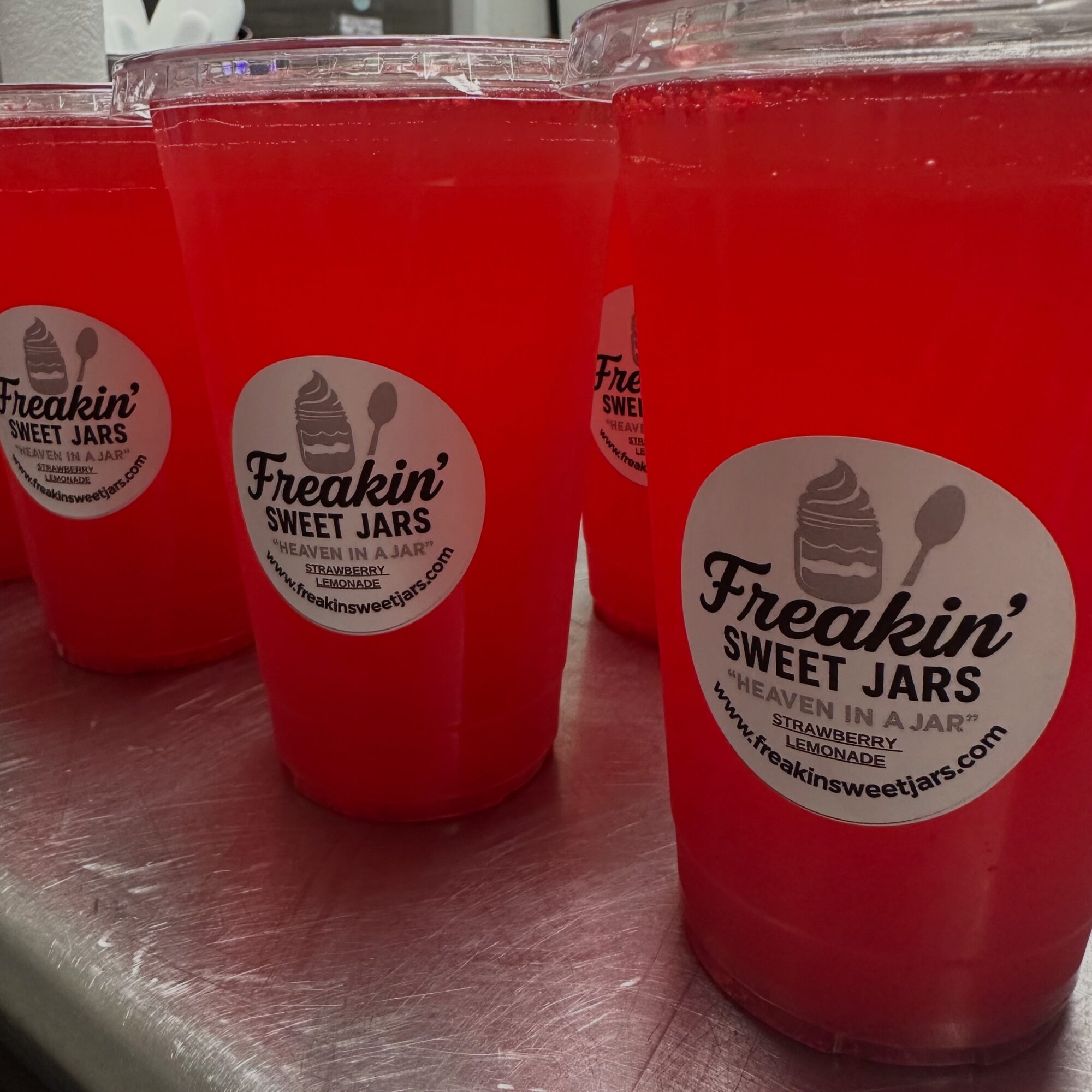 Three red drinks in clear cups with a label reading 'Freakin' Sweet Jars' on a table.