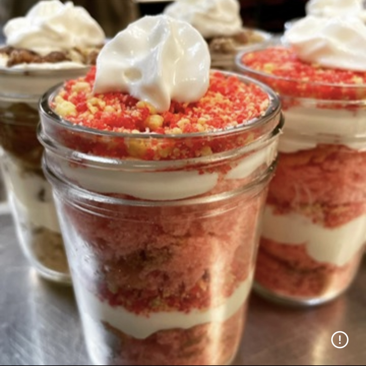 Layered dessert in a glass jar with red, white, and pink layers topped with whipped cream and crumbs.