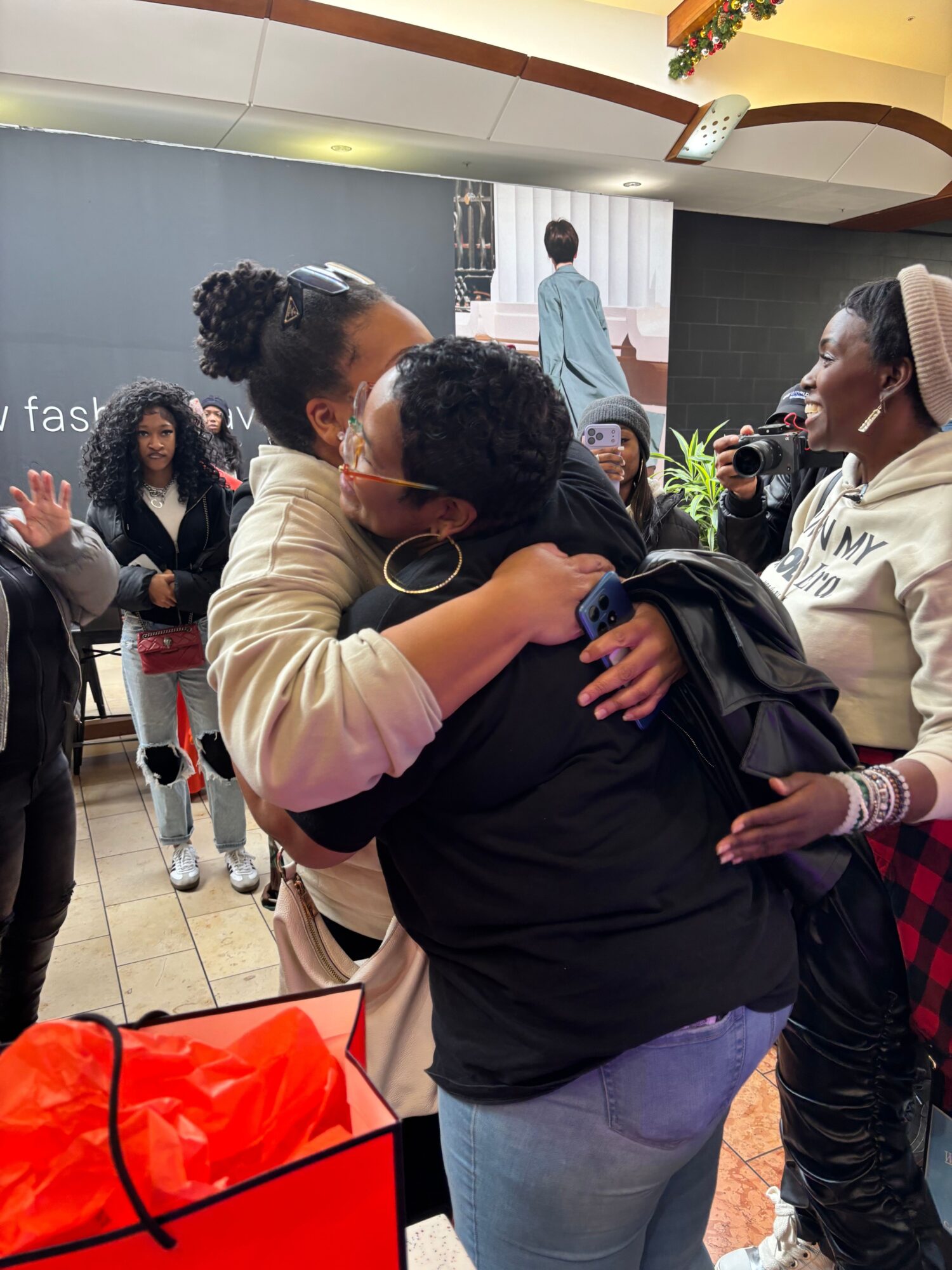 People gathered indoors, some hugging, others talking, with a bright, modern interior background.