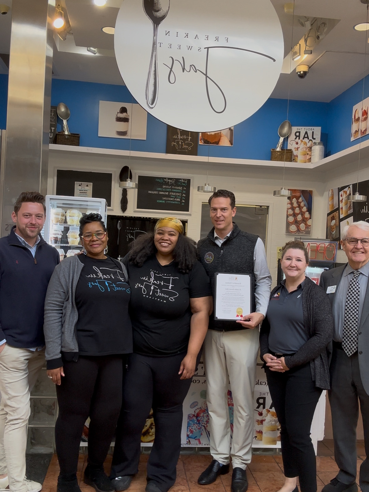 Group of five people standing inside a store, smiling, with shelves and products behind them.