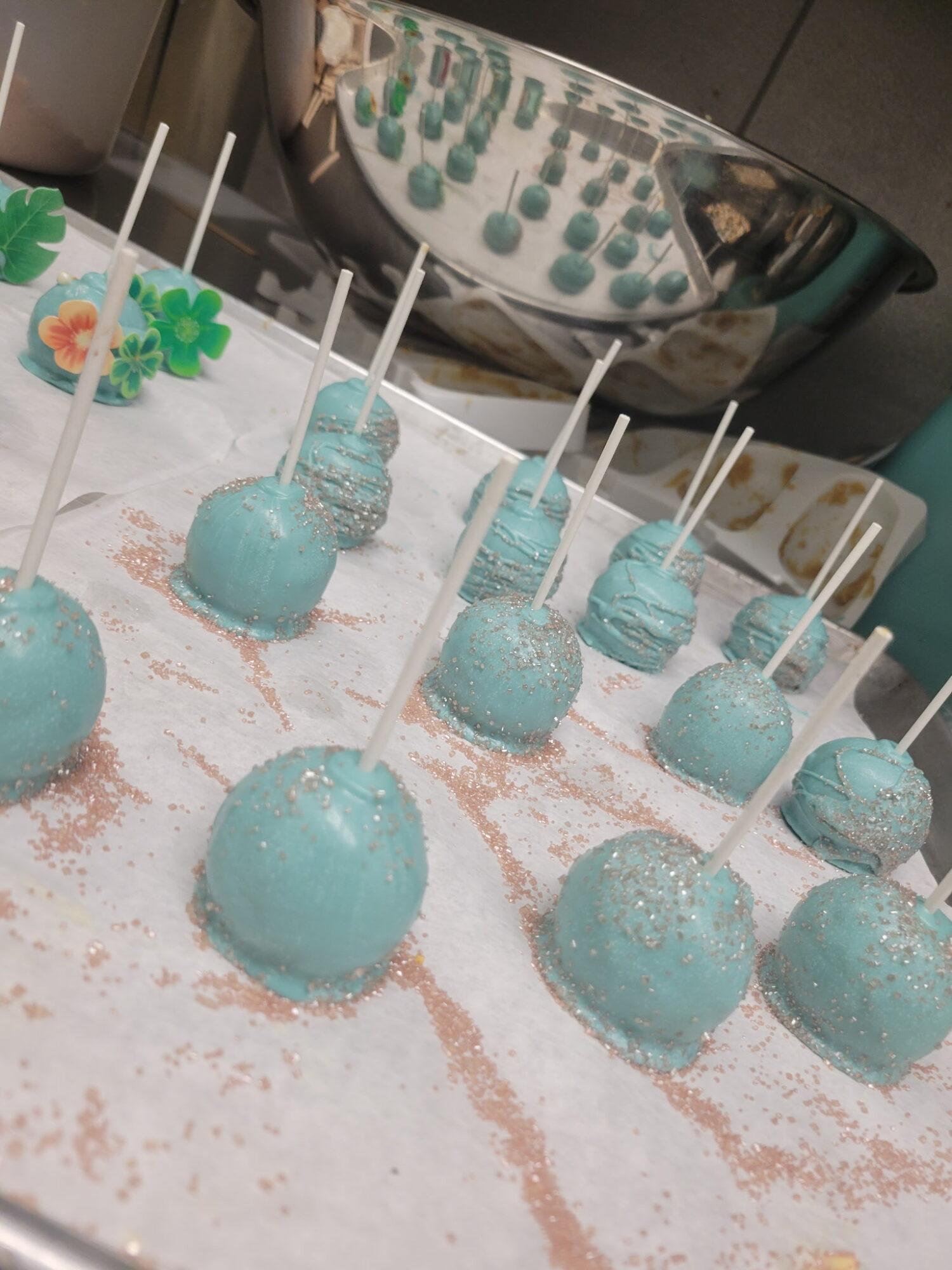 Blue cake pops with white sticks arranged on a surface with pink sprinkles, and a fish-shaped object in the background.