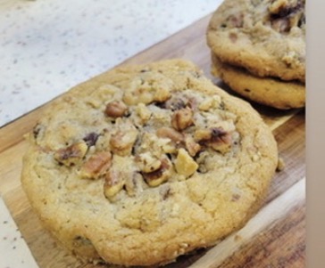 Two cookies with nuts and chocolate chips on a wooden surface, one in the foreground and one in the background.