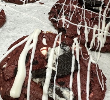 Chocolate cookies with white icing drizzled on top, placed on parchment paper.