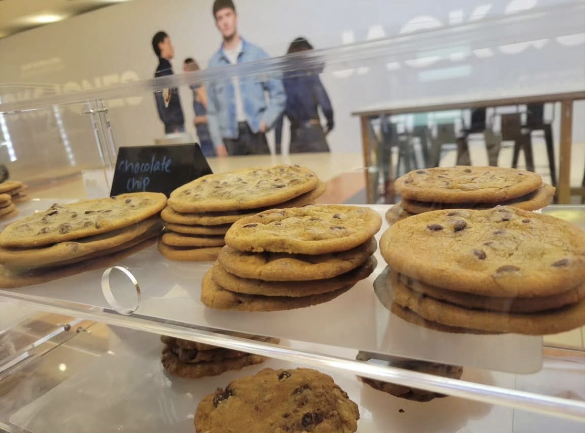 Stacks of chocolate chip cookies on a glass display counter with people in the background.