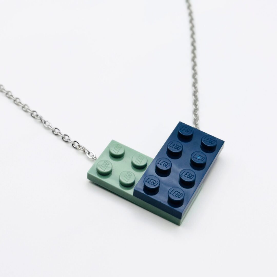 Necklace with a pendant made of two LEGO bricks, one light green and one dark blue, connected at a right angle, on a white background.