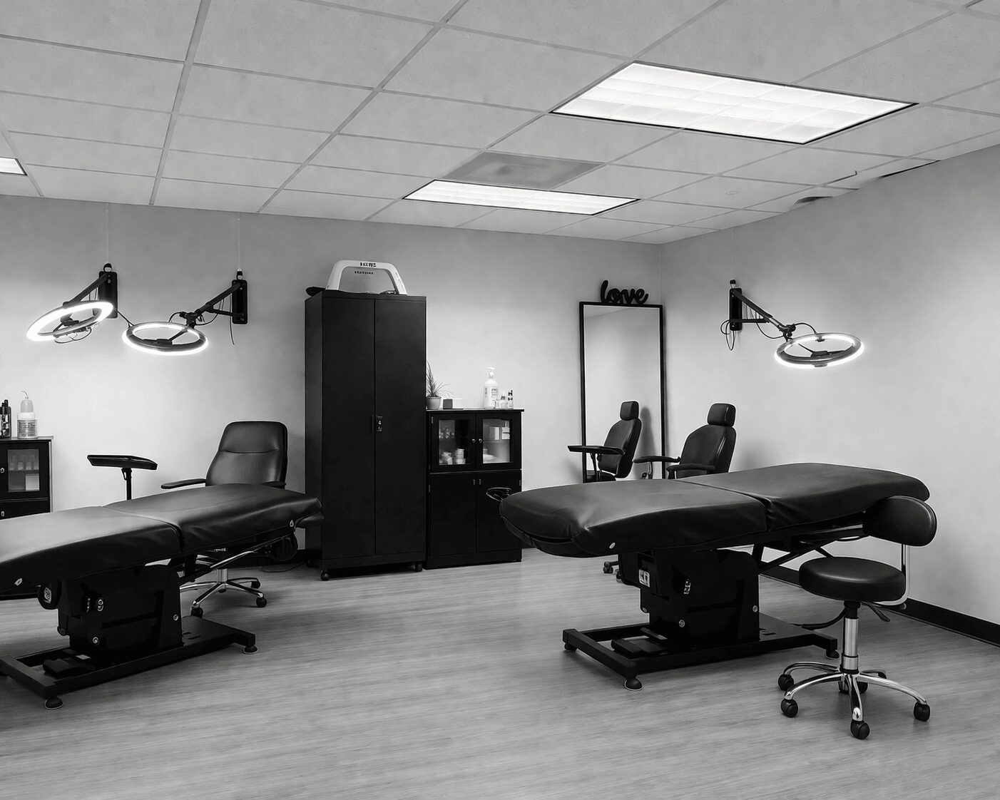 Medical examination room with two examination tables, chairs, cabinets, and overhead lights, arranged neatly in a clinical setting.