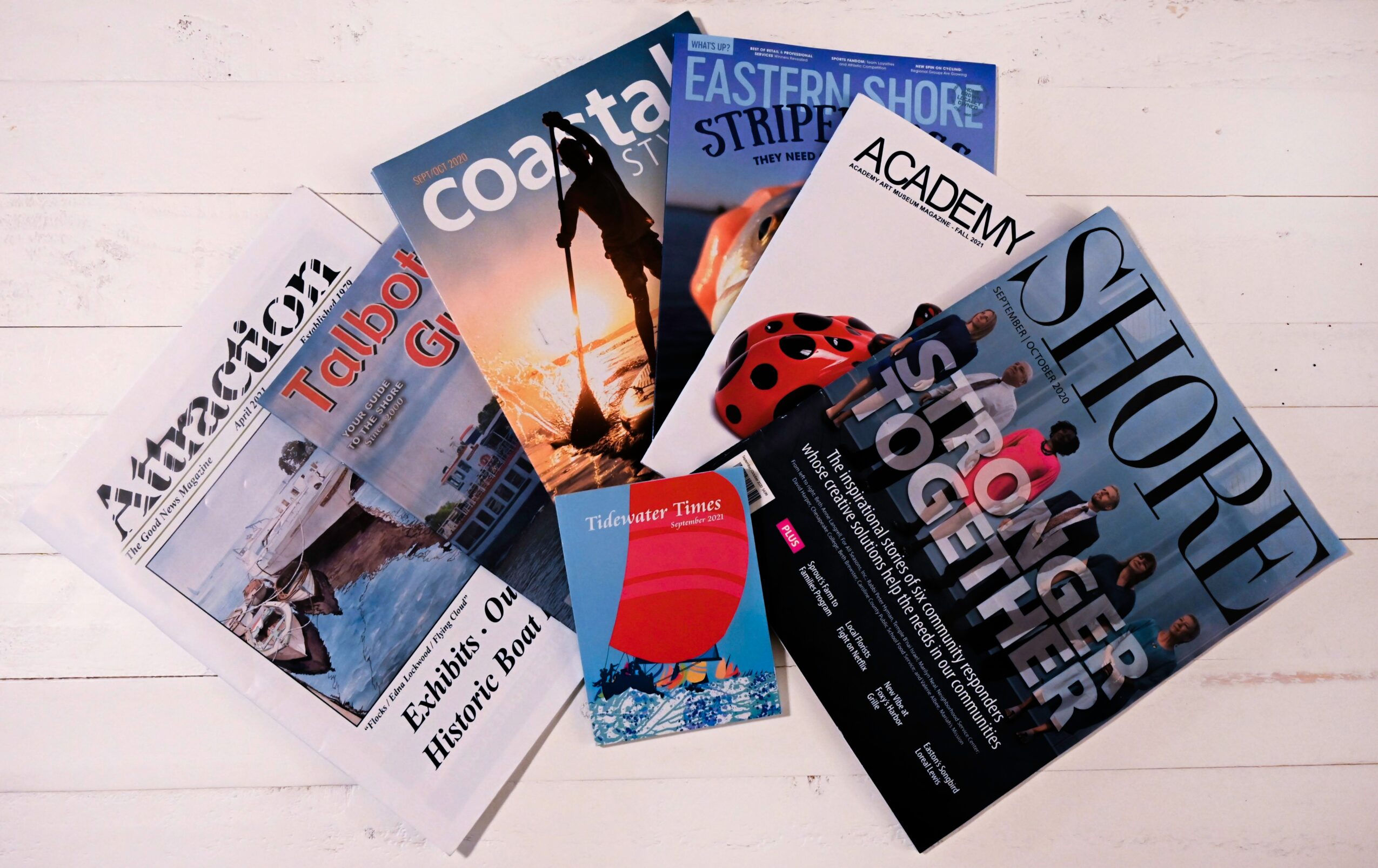 Six magazines and a small booklet fanned out on a white surface, featuring various covers and titles.