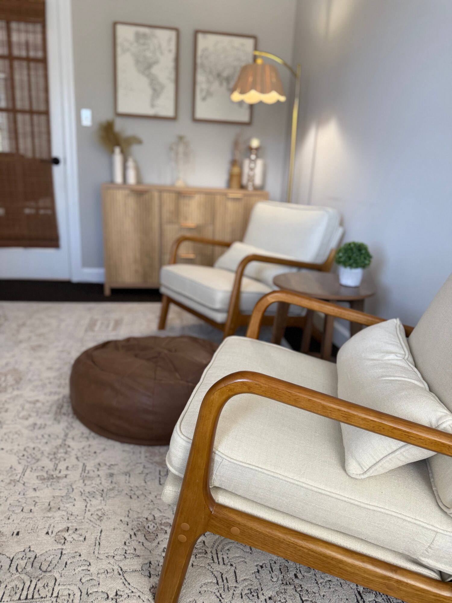 Living room corner with white armchair, wooden frame, and a small side table with a plant, against a light wall.