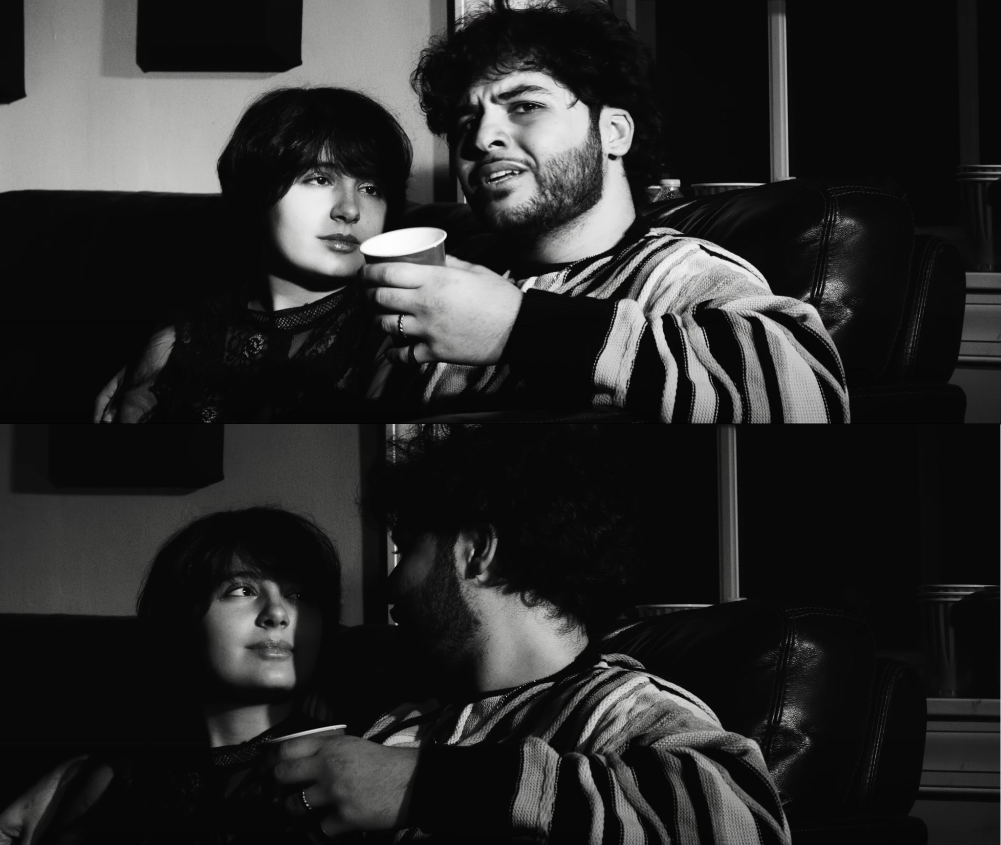 A man and a woman sit together on a couch, the man holding a cup, in a black and white photo.