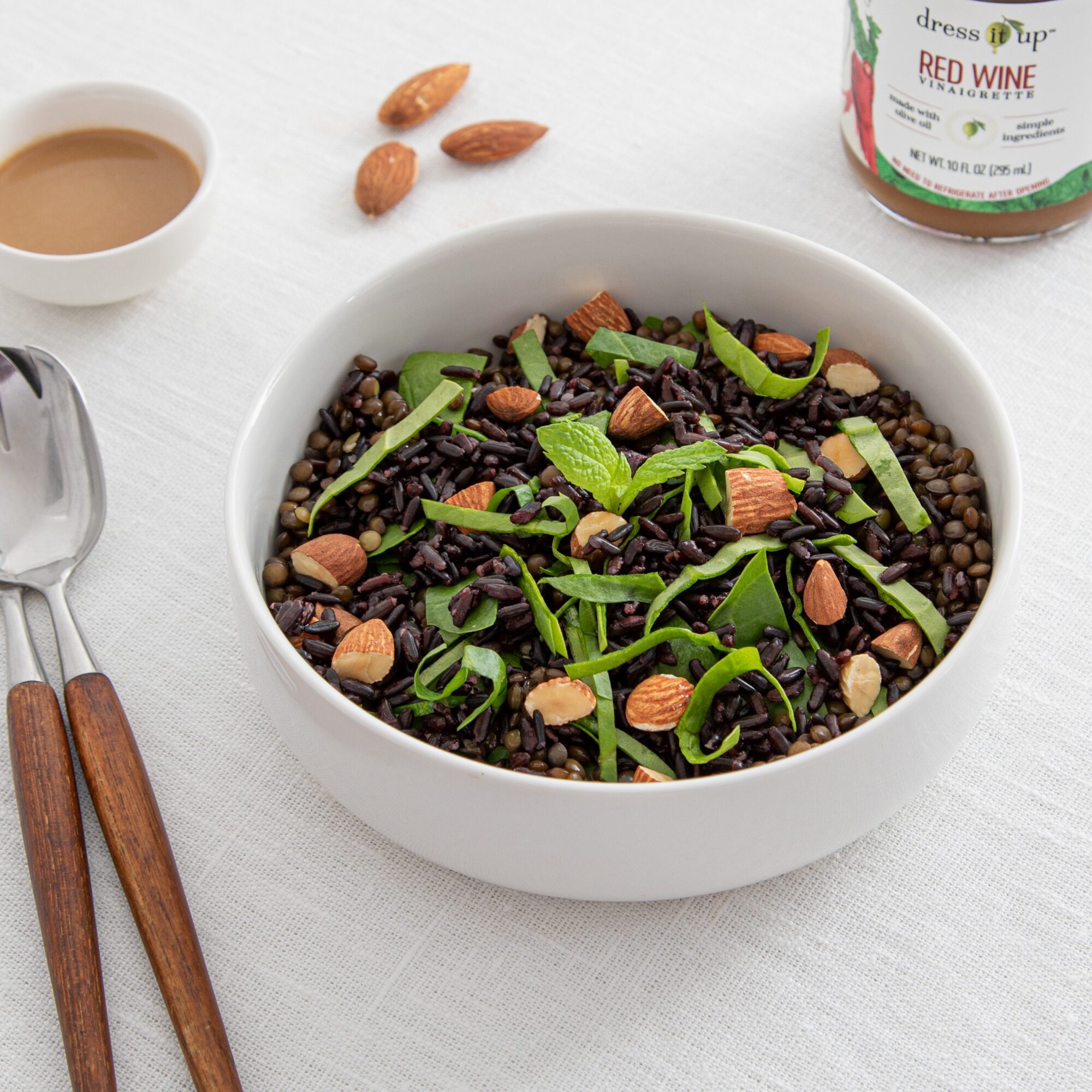 White bowl filled with black lentil salad topped with chopped almonds and green herbs on a white surface.