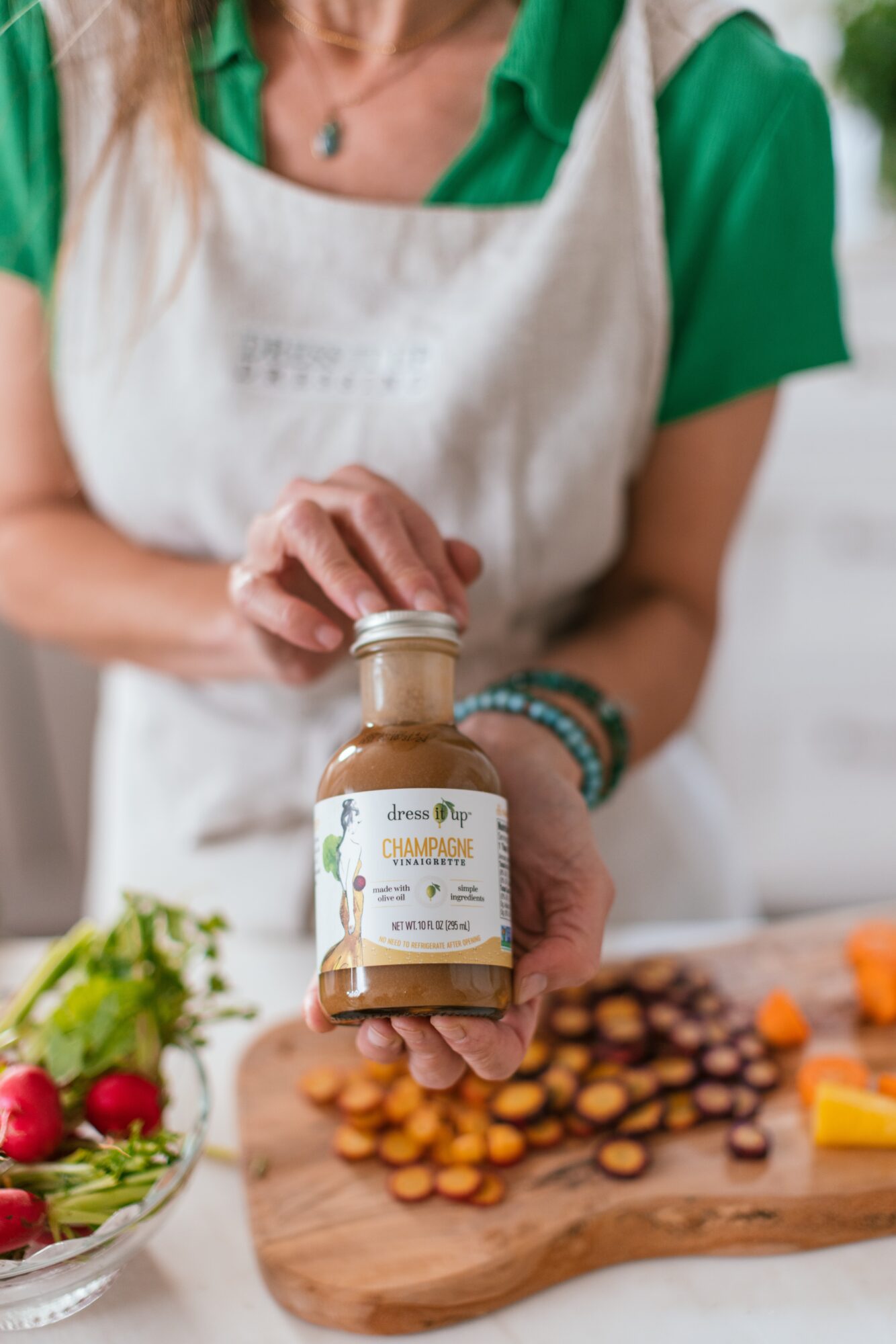 Person holding a small jar of sauce in a kitchen, with a cutting board and vegetables in the background.