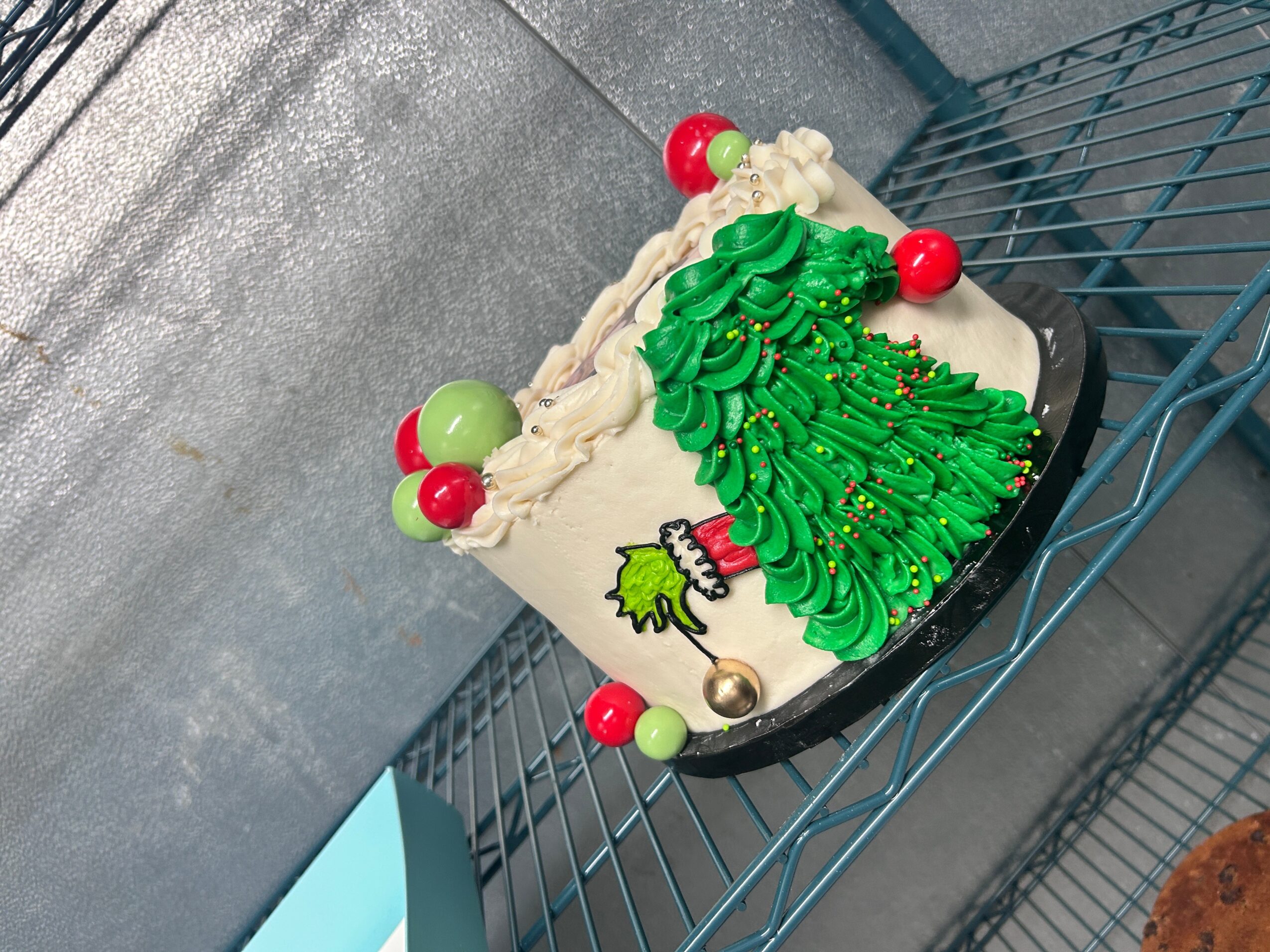 Christmas-themed cake with green frosting shaped like a tree, red and green decorations, and a small Santa figure, on a wire shelf.