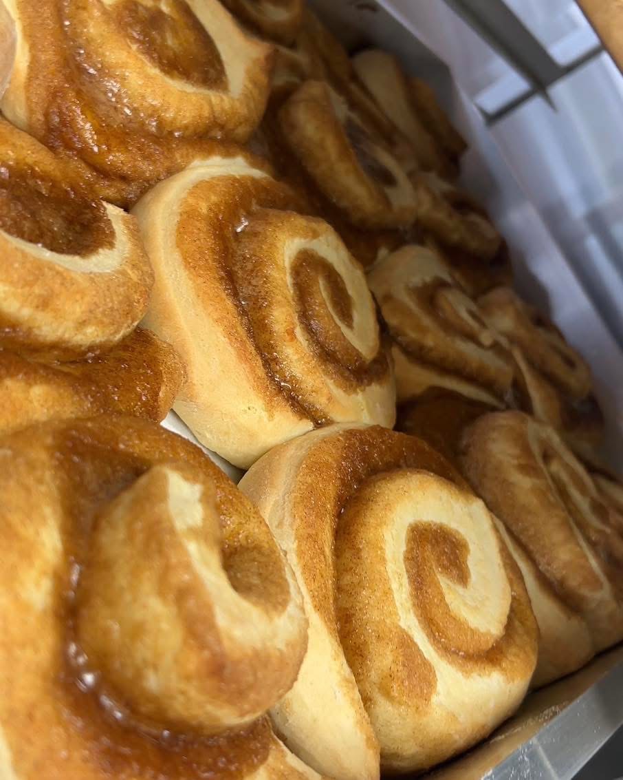 Close-up of cinnamon rolls with swirled pattern, golden-brown tops, and soft interior, piled together in a tray.