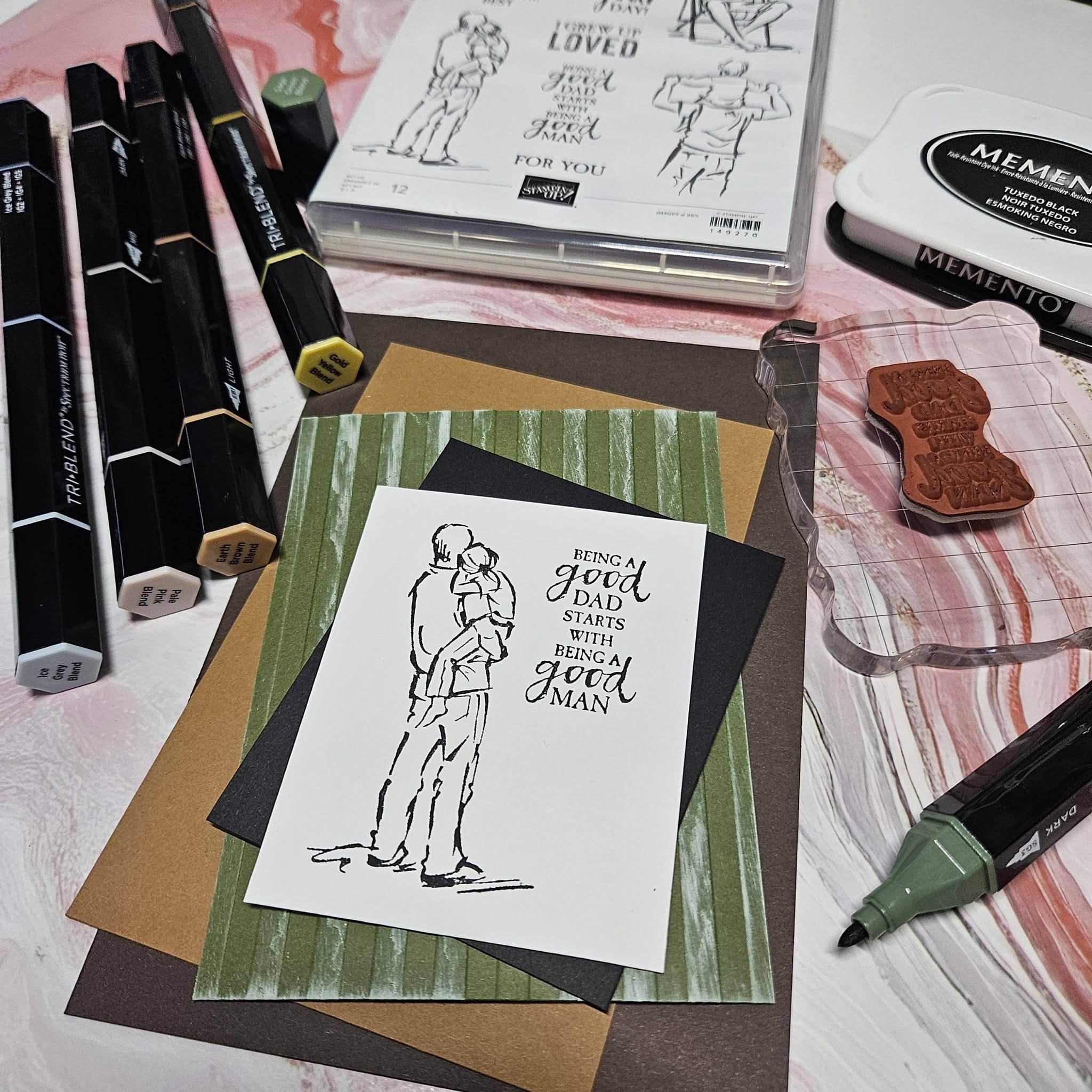 Art supplies including markers, ink pads, and paper with sketches and cards on a table.