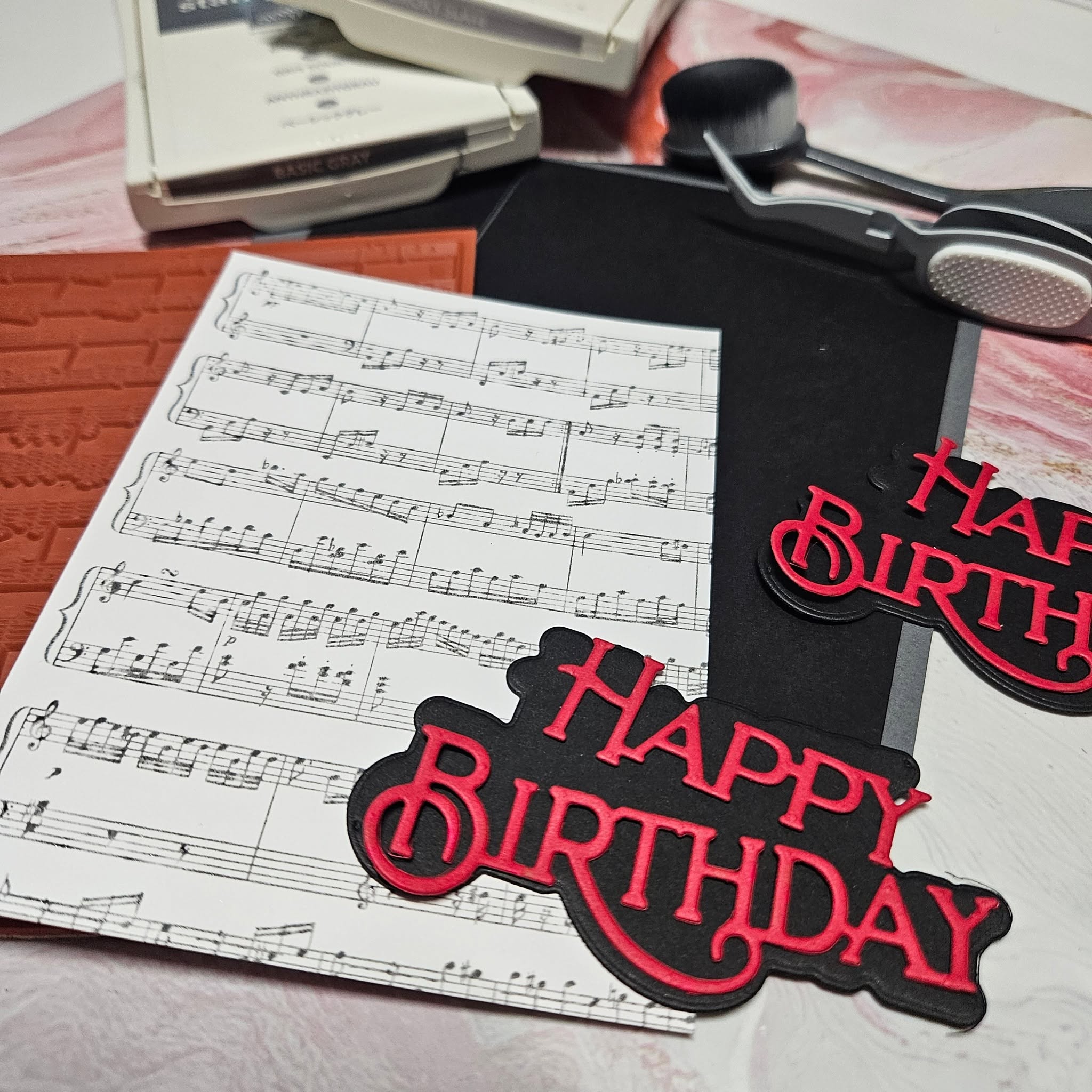 Sheet music, birthday decorations, and a black and pink 'Happy Birthday' sign on a table.
