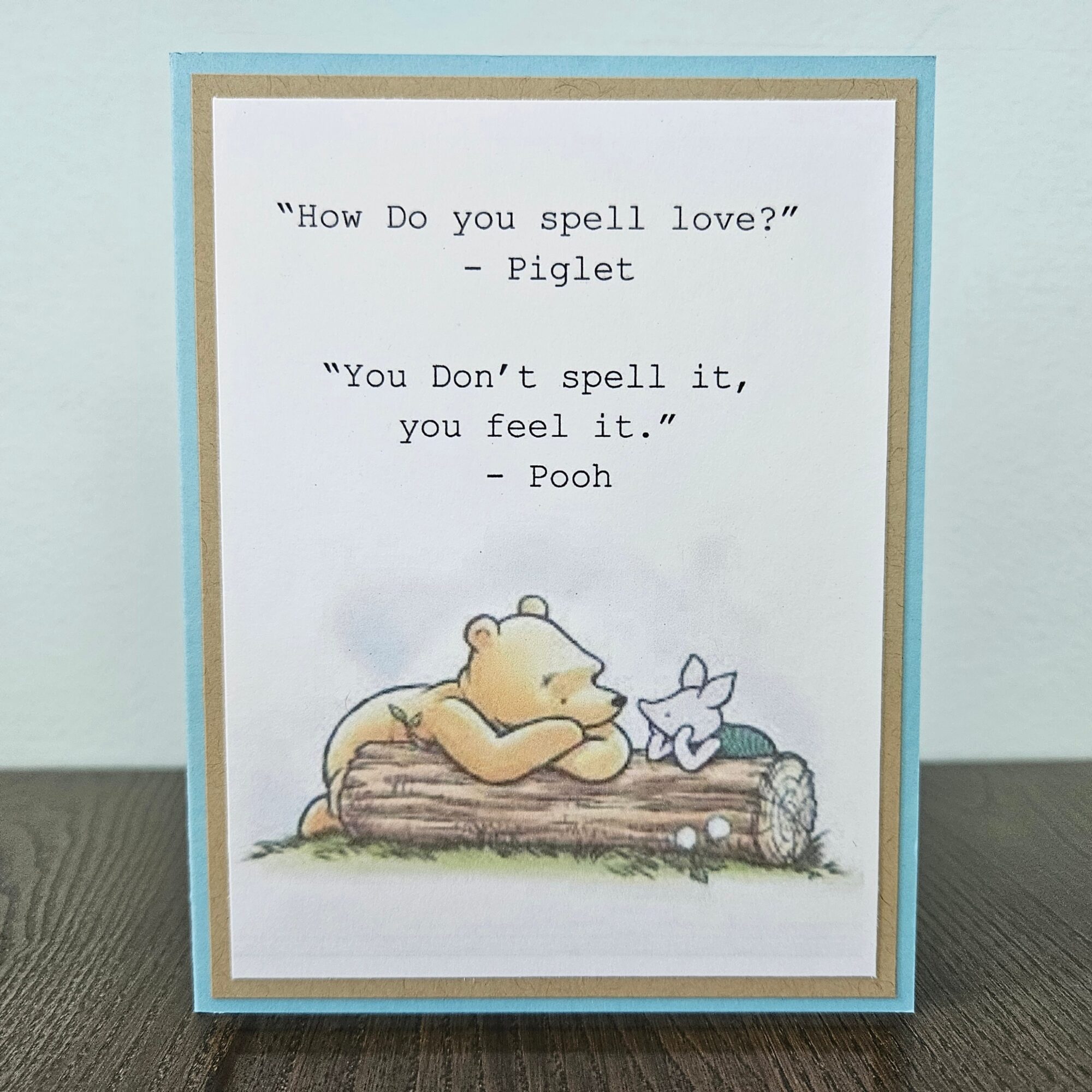 A greeting card with a quote from Piglet and Pooh, featuring a bear and a piglet resting on a log, on a light blue background.