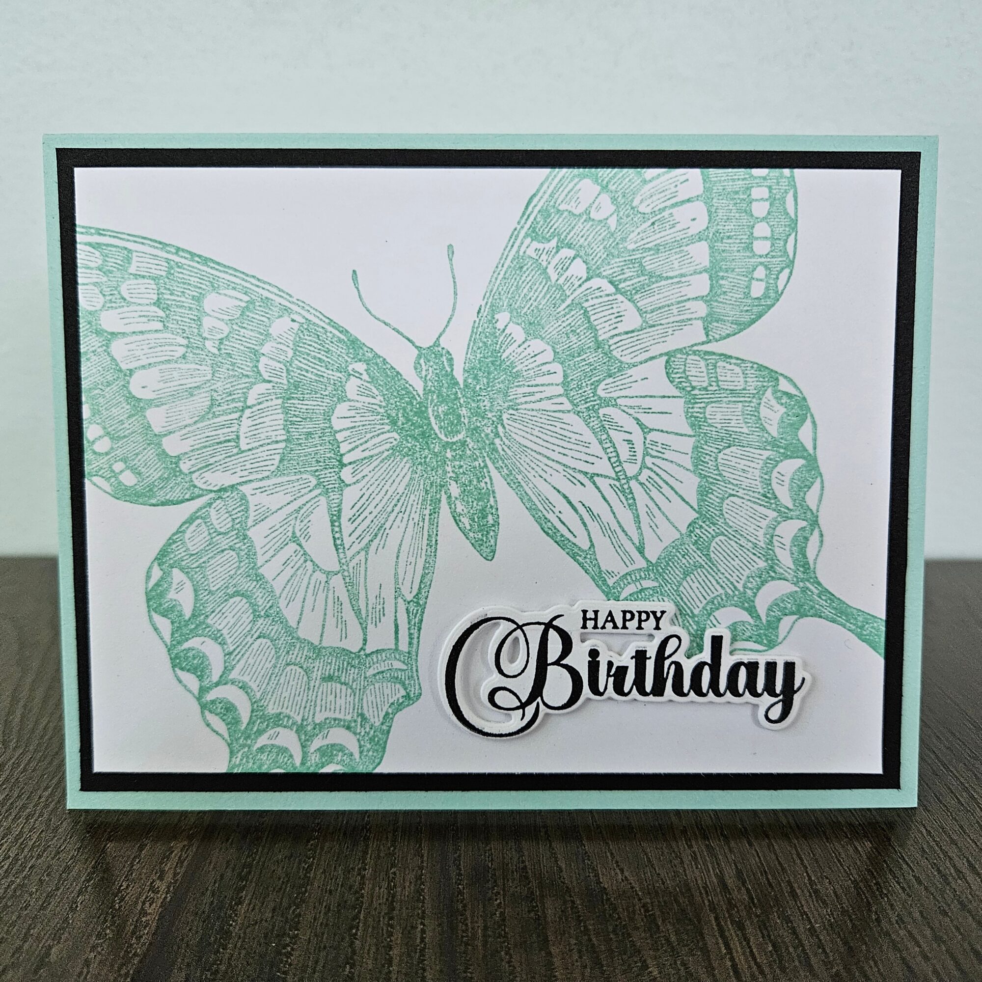 A birthday card with a large green butterfly illustration and a 'Happy Birthday' message, on a wooden surface.