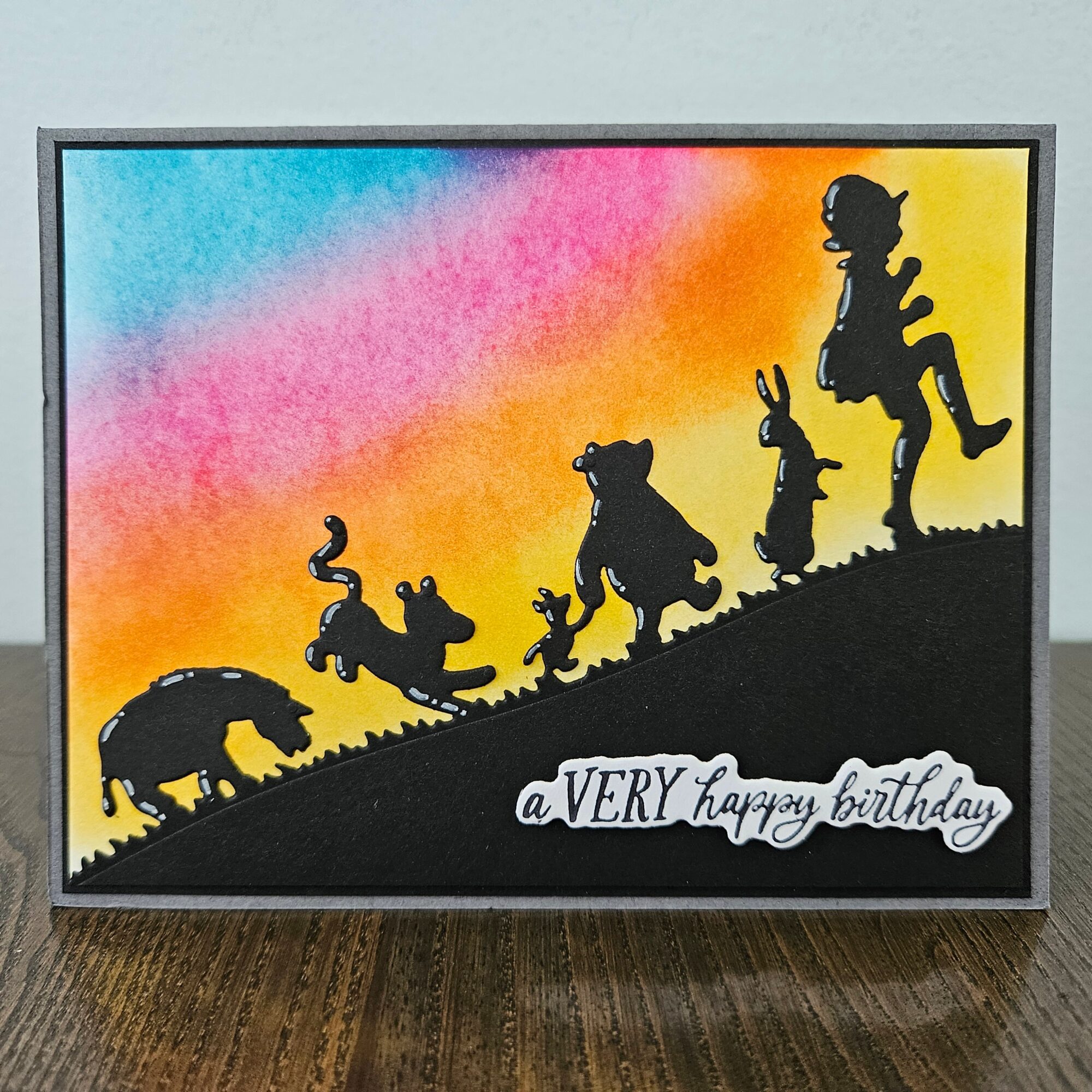 Silhouettes of animals and a person on a hill with a colorful sky background, birthday message at the bottom.