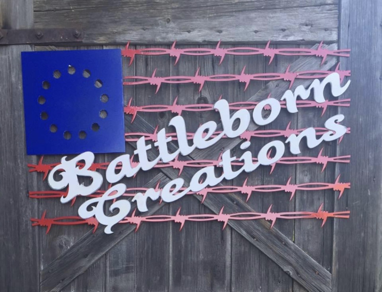 Sign with white text reading 'Battleborn Creations' on a wooden background, decorated with pink and red barbed wire designs.