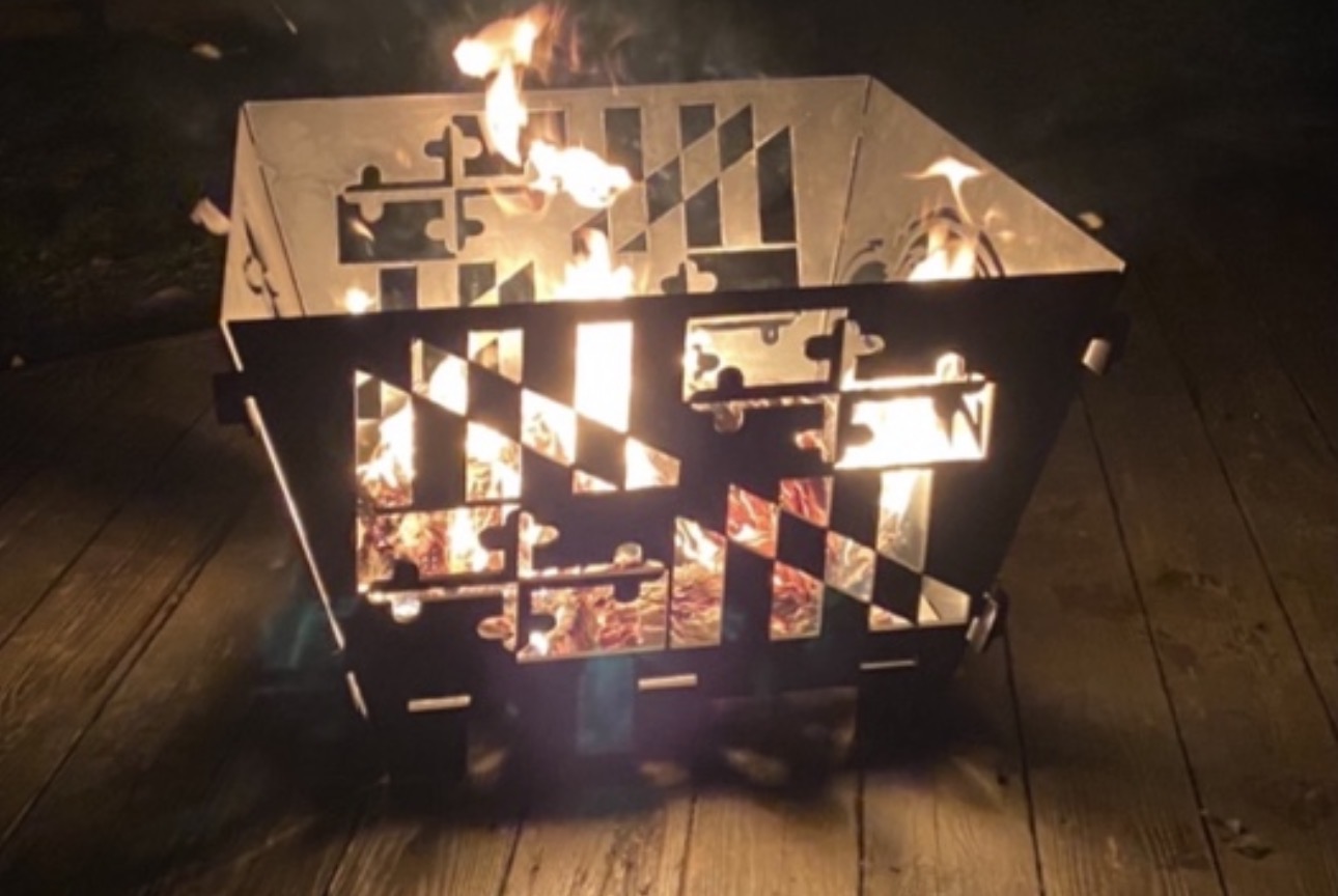 Metal fire pit with flames, placed on a wooden surface at night, with visible fire inside.