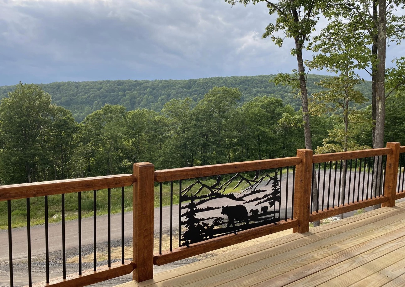 Wooden deck with railing overlooking a forested landscape and cloudy sky.