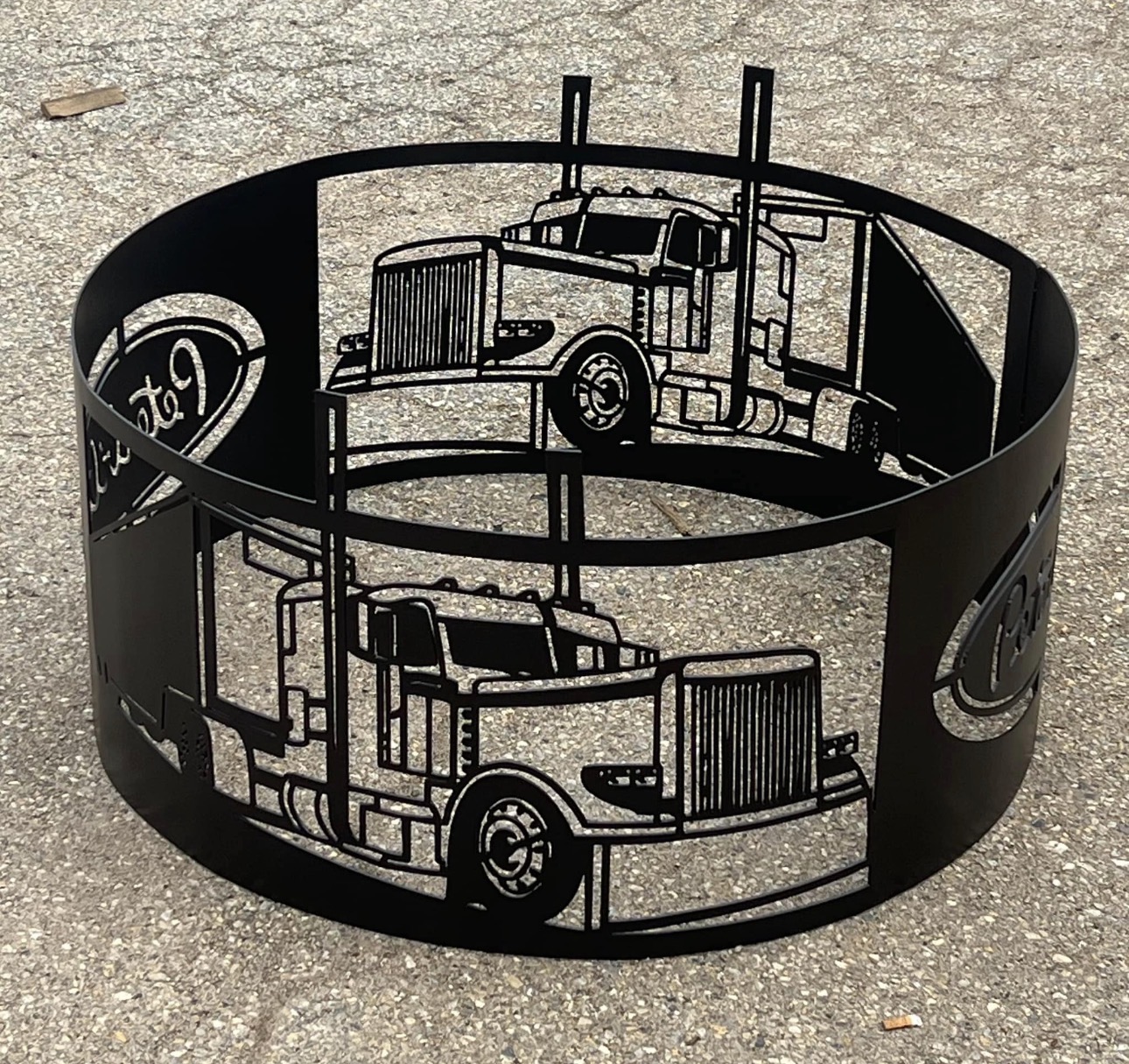 Circular metal band with truck illustrations, placed on a rough surface, with visible logos on the sides.